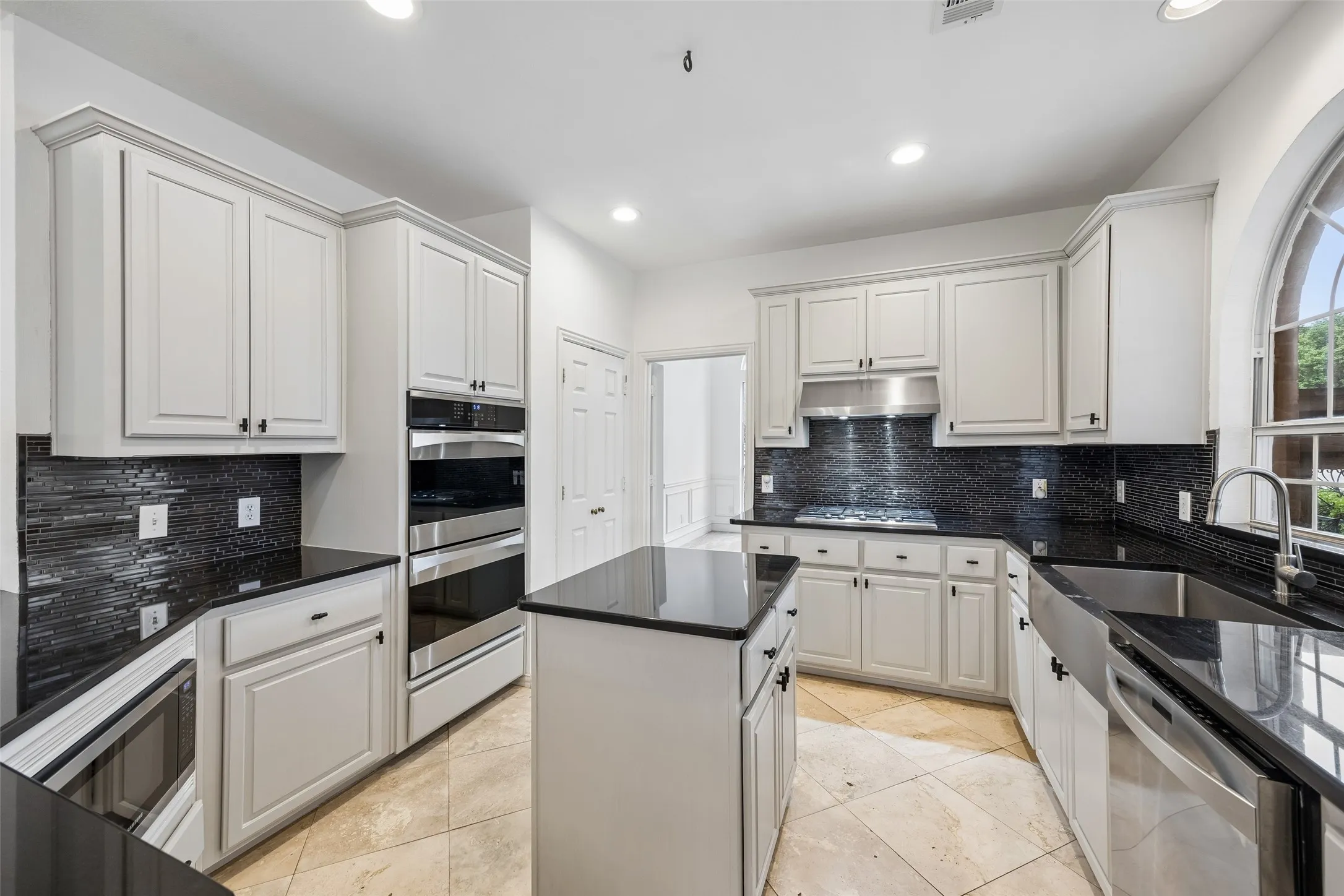 Bright kitchen featuring gray cabinetry, black countertops, a mosaic tile backsplash, stainless steel appliances, and a central island