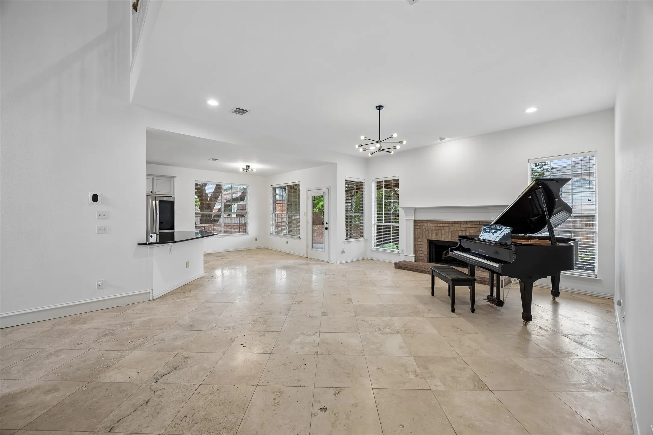 Spacious open-concept living area featuring a fireplace with a brick surround, white mantle, multiple windows, and a built-in breakfast bar with a dark countertop