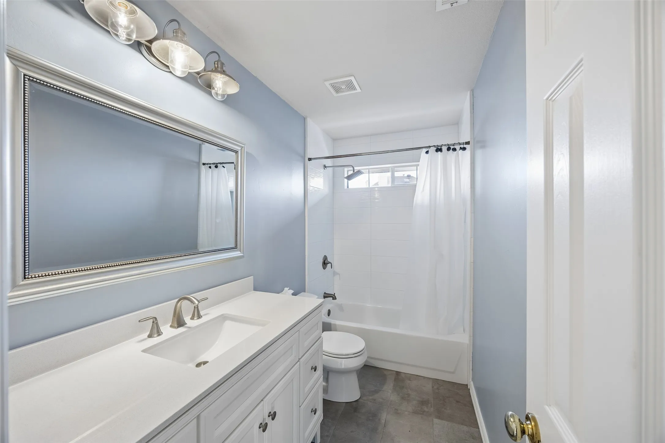 Bathroom featuring a white vanity with an integrated sink and brushed nickel faucet, framed rectangular mirror, and three-light fixture