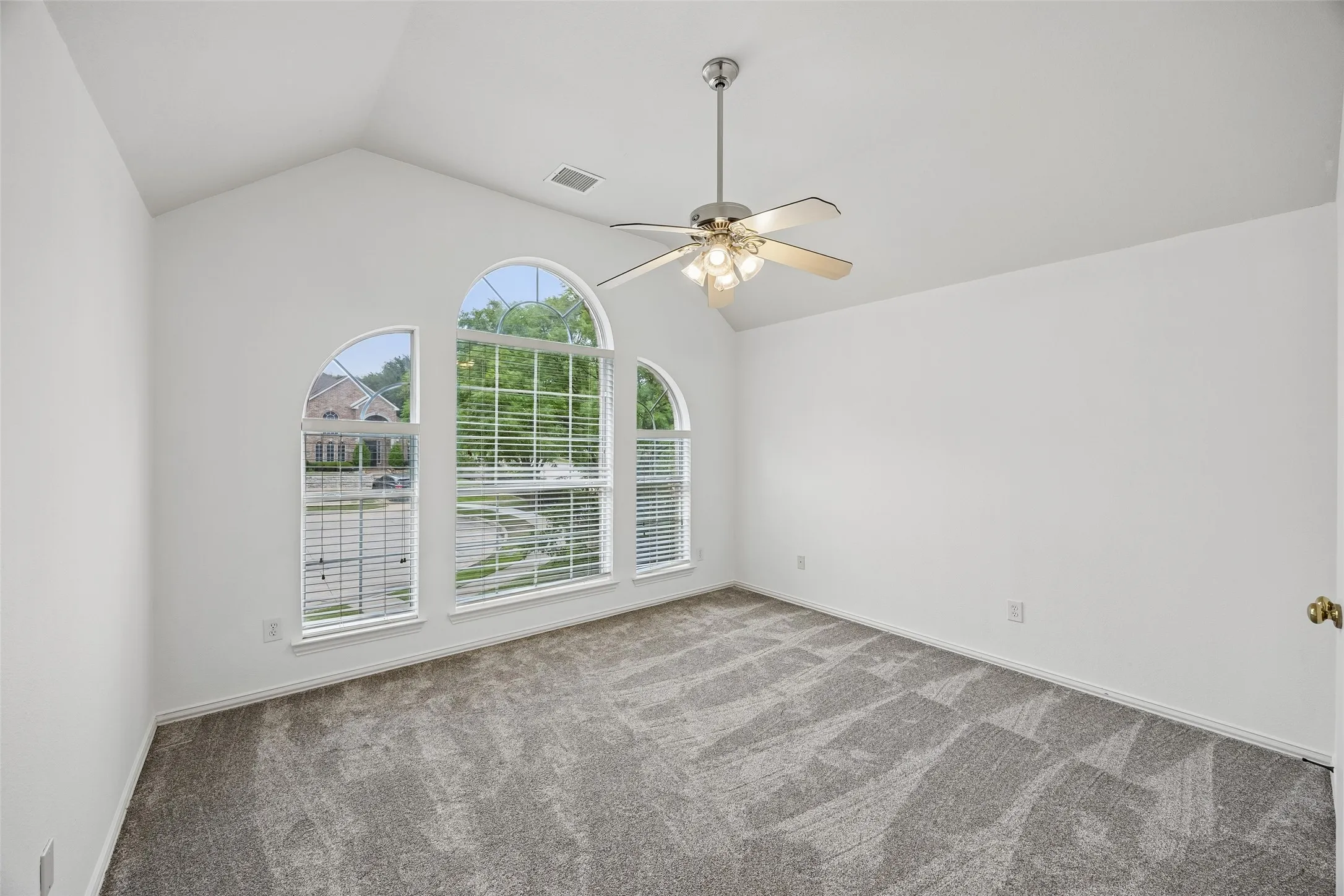 Vaulted ceiling room featuring three arched windows, a ceiling fan with integrated lighting, and neutral-toned carpet