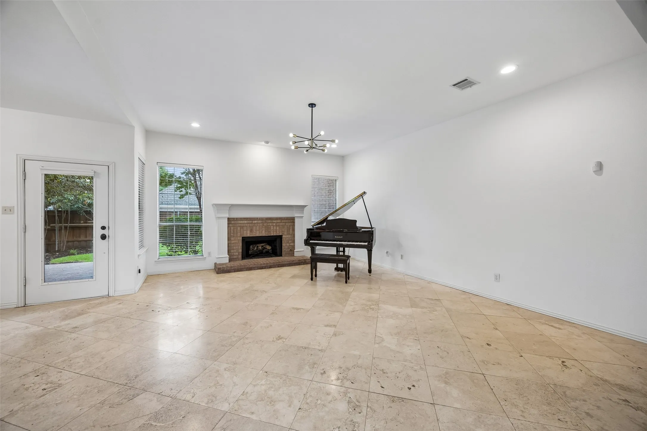 Spacious room featuring a brick fireplace with a white mantel, and a contemporary multi-arm chandelier