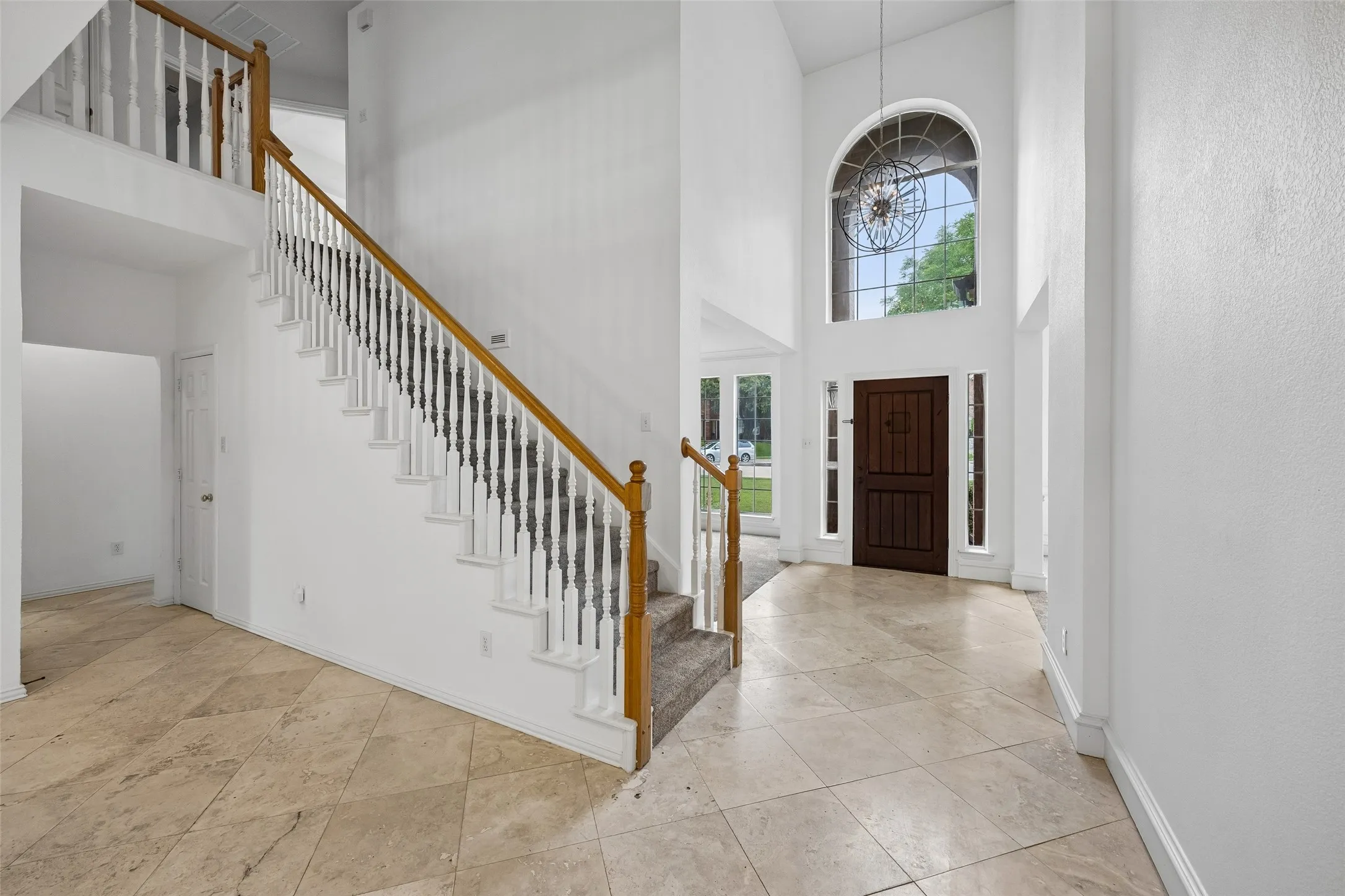 Two-story foyer featuring an arched window, a dark wood entry door with flanking sidelights, and a grand staircase with wood handrails