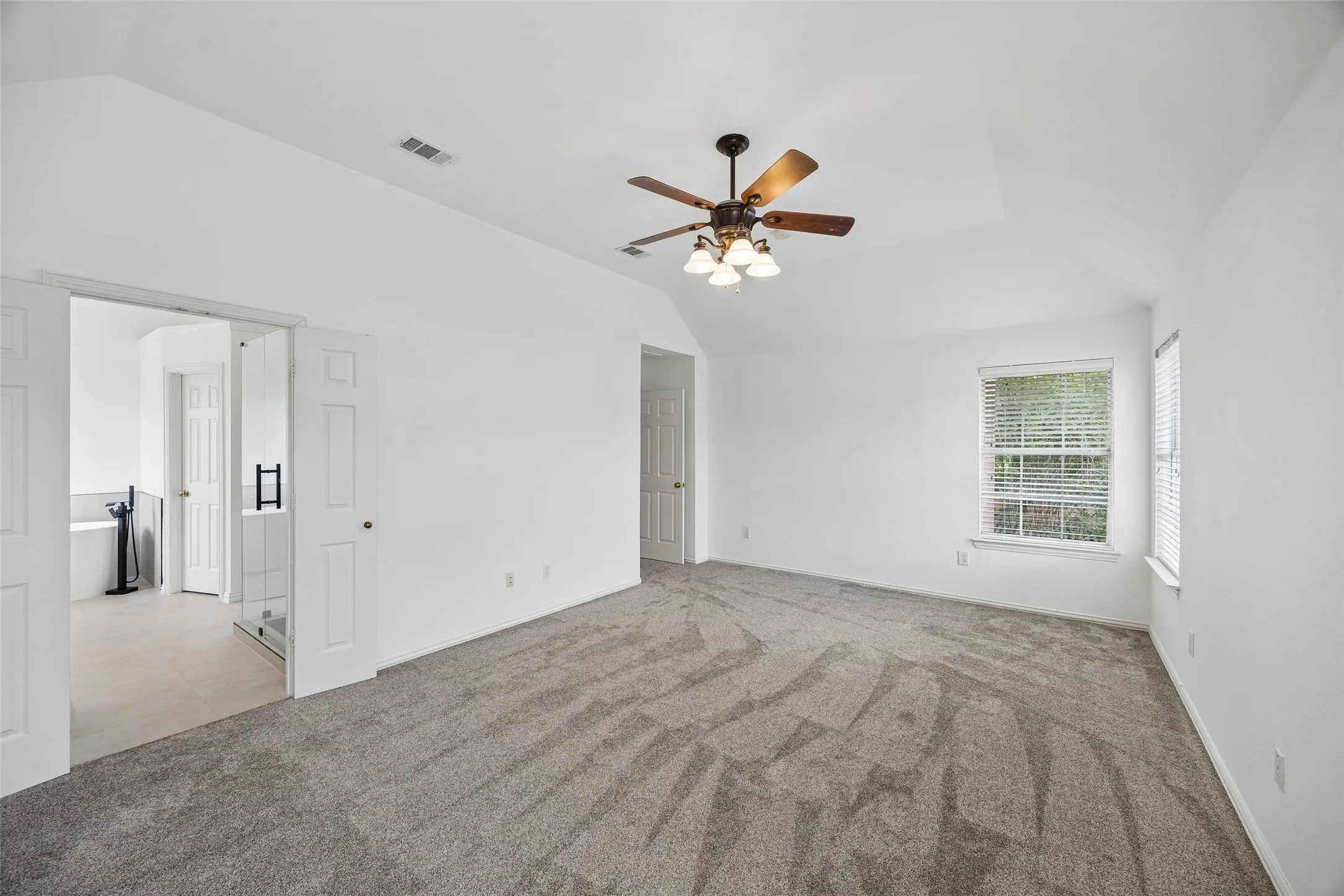Spacious carpeted room featuring a ceiling fan with integrated lighting, vaulted ceilings, and white painted walls