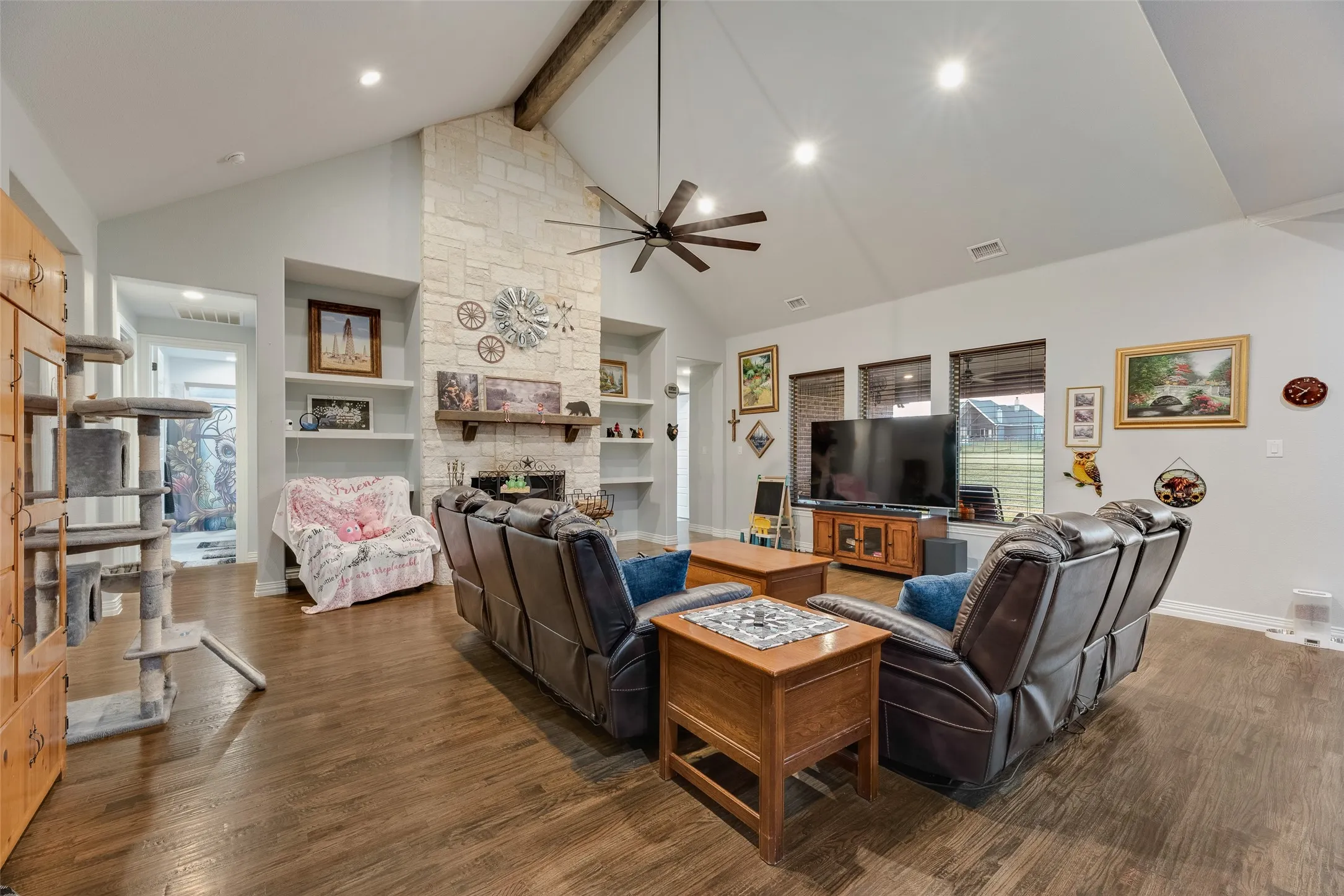 Spacious living area featuring a vaulted ceiling with exposed wood beam, wood-finish flooring, and a stone-clad fireplace