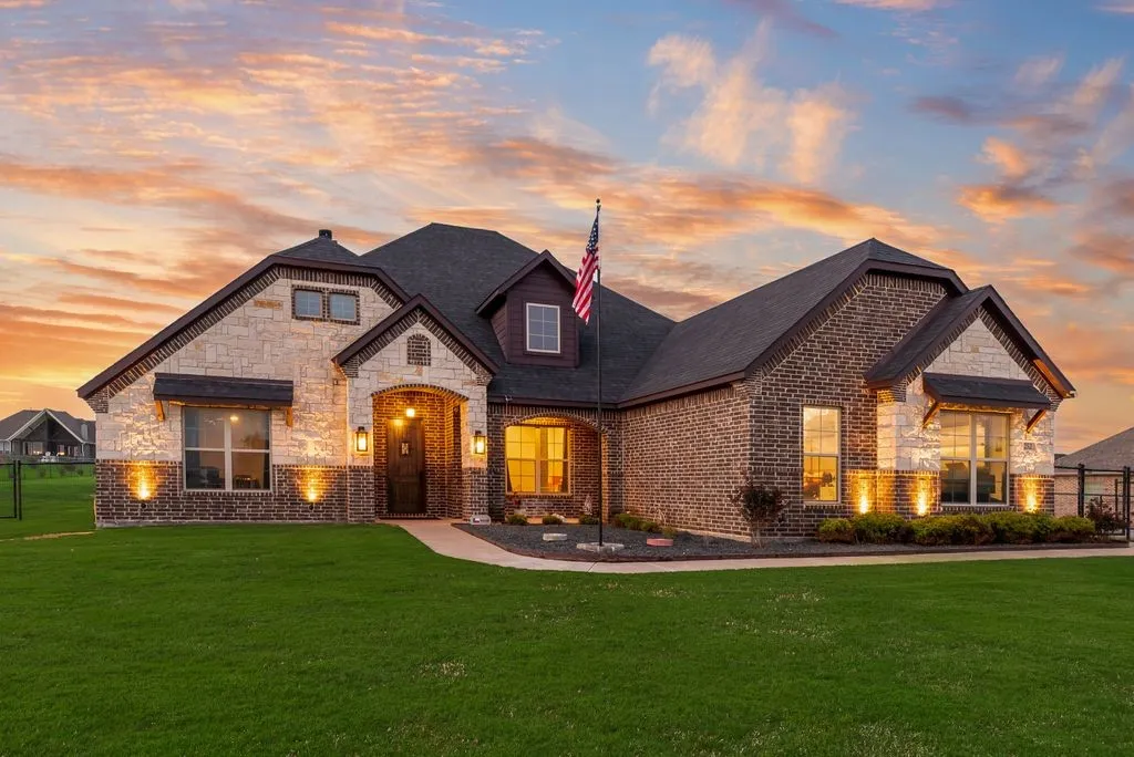 Brick and stone facade residence featuring a dark shingle roof and a green lawn