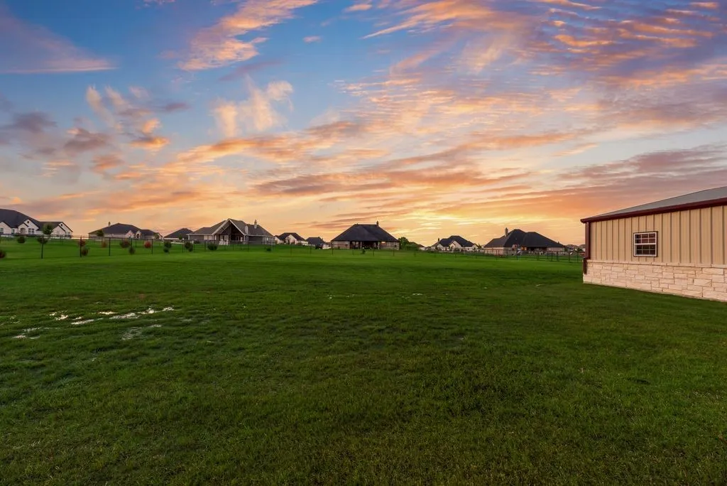 Expansive green lawn with a large outbuilding featuring horizontal siding and a stone-clad foundation