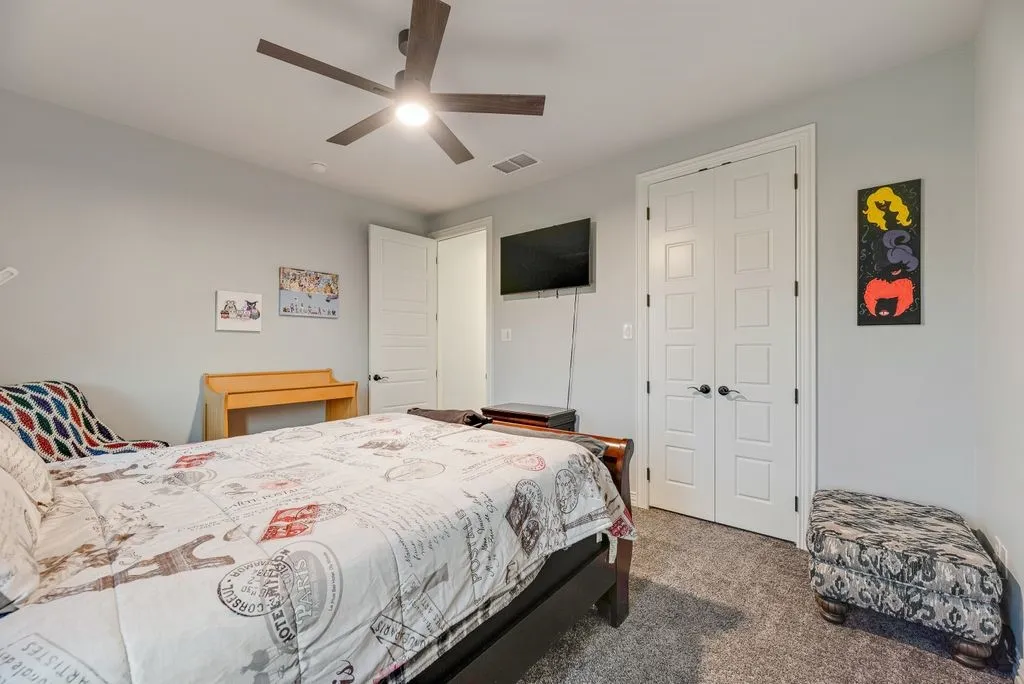 Interior room featuring light gray walls, textured gray carpeting, a multi-blade ceiling fan with integrated lighting, and white paneled doors