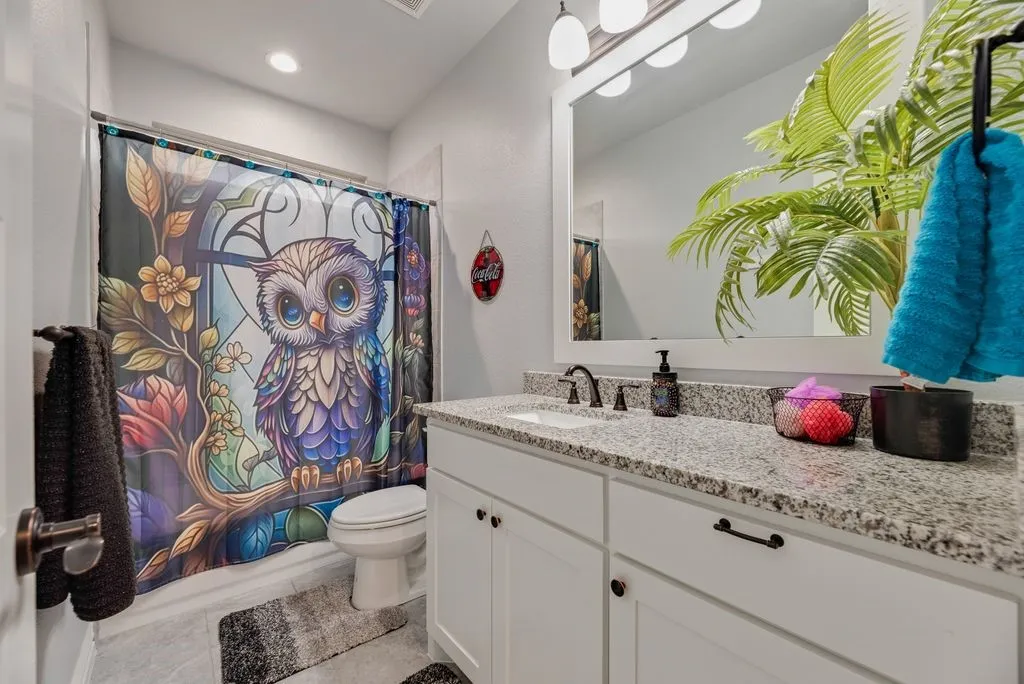 Bathroom featuring a white vanity with granite-finish countertop, undermount sink, and dark-finish faucet