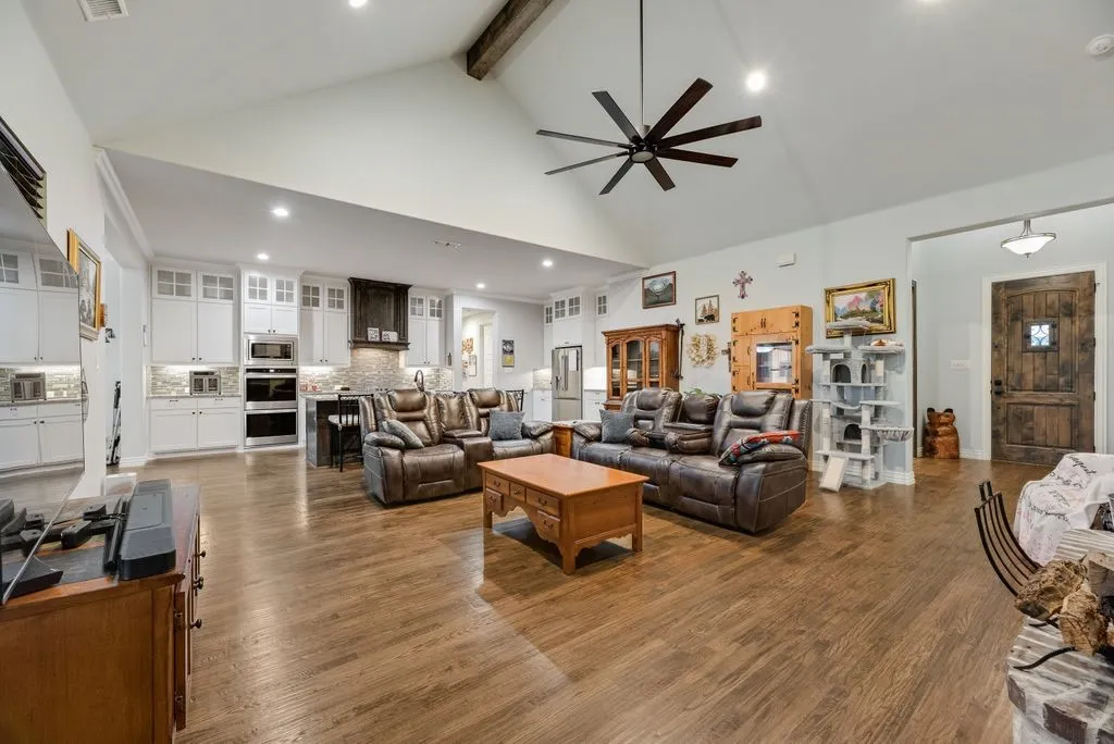 Expansive open-concept living space featuring vaulted ceilings with exposed beam, wood-finish flooring, recessed lighting, and a large ceiling fan