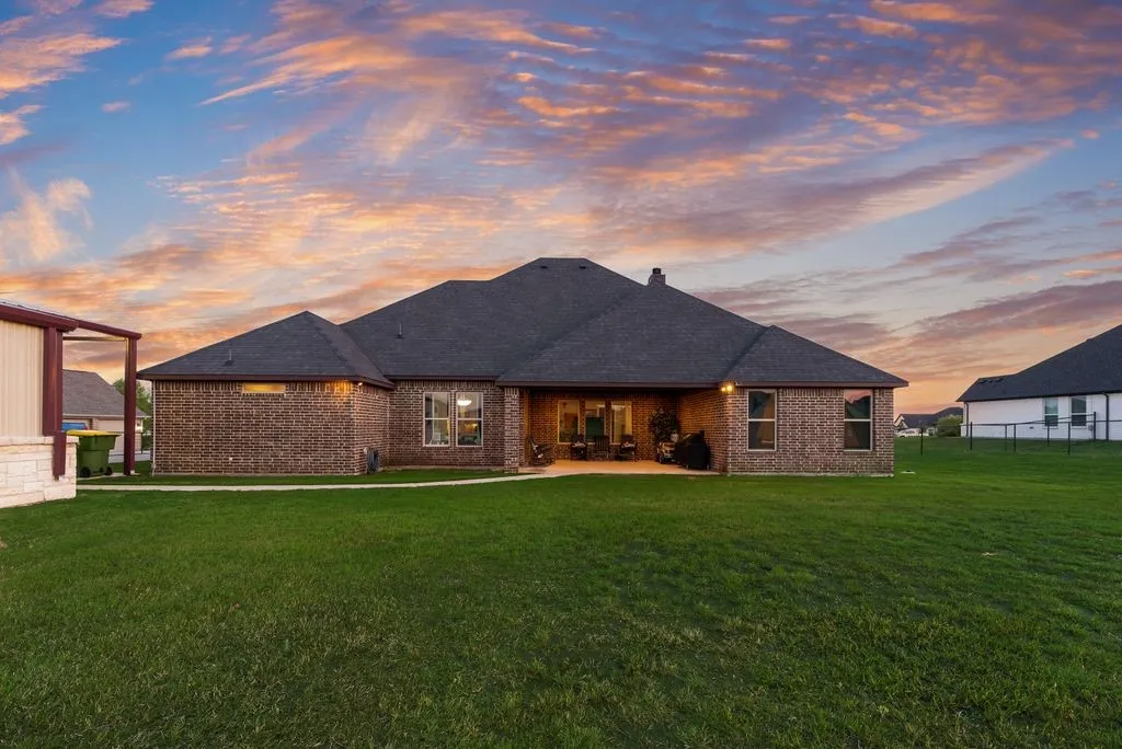 Expansive rear exterior featuring a covered patio, brick facade, and a dark shingle roof