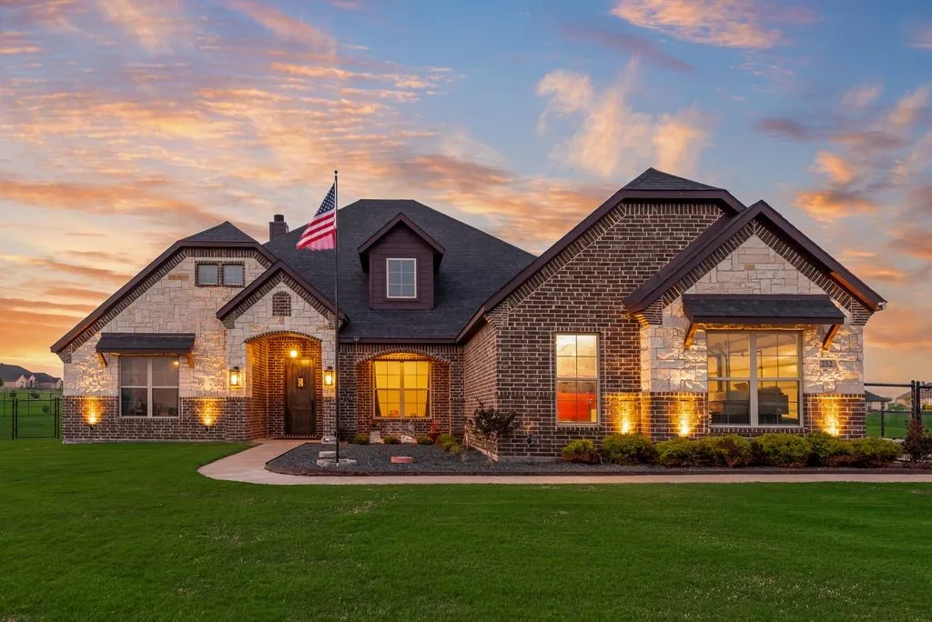 Brick and stone facade residence featuring a dark shingle roof and a prominent front entrance