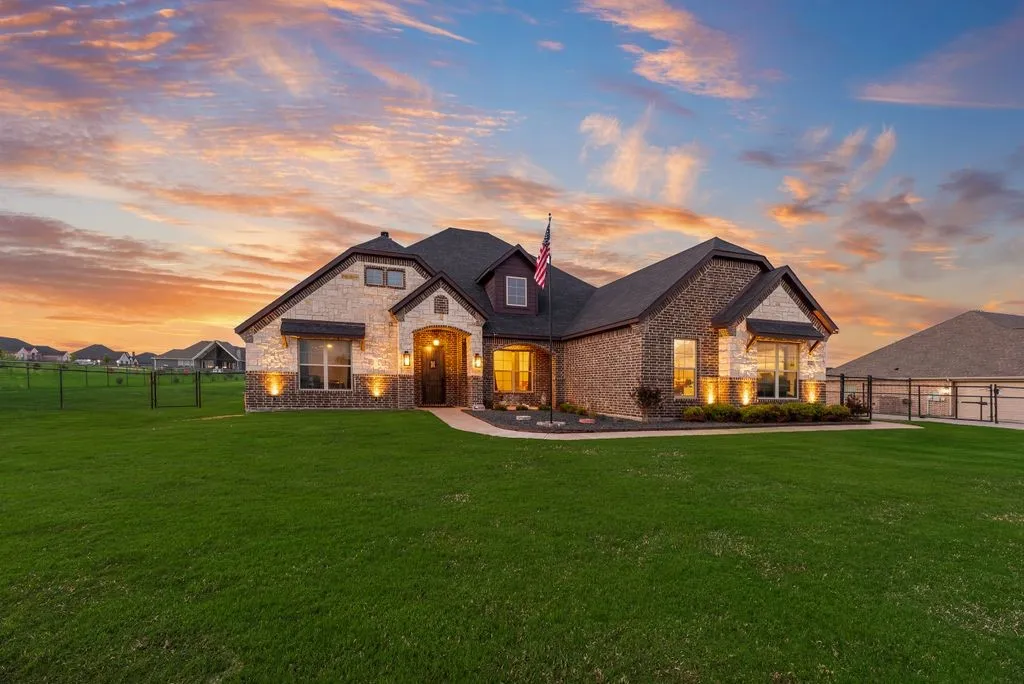 Exterior featuring a combination of brick and stone masonry, arched entryway, manicured lawn, architectural shingles, and exterior accent lighting