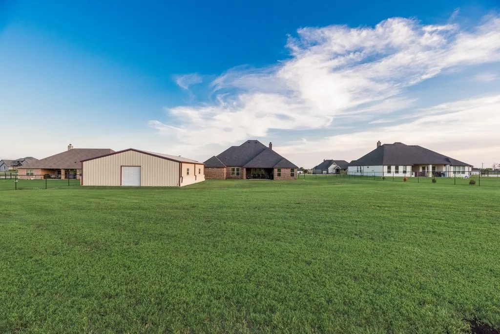 Expansive green lawn with a large, light-colored metal outbuilding featuring a roll-up door