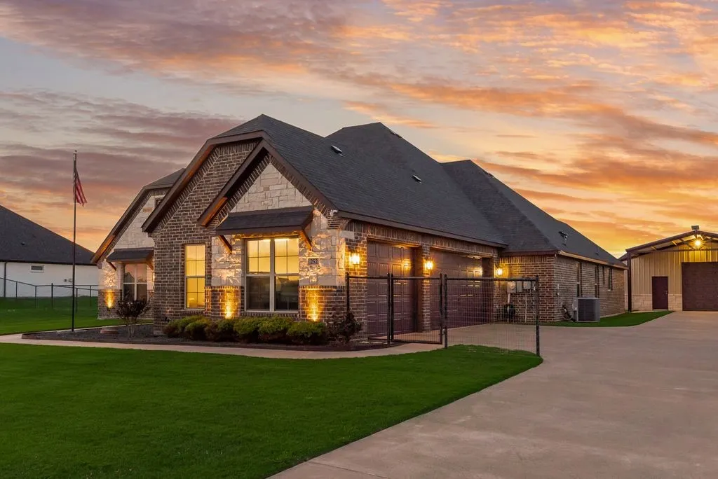 Brick and stone facade residence featuring a dark shingle roof and multiple gables