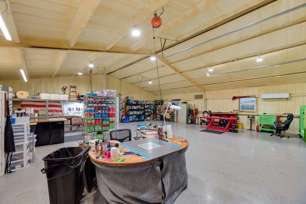 Spacious workshop featuring a high vaulted ceiling with exposed beams, industrial-grade lighting, durable concrete flooring, and a wall-mounted air conditioning unit