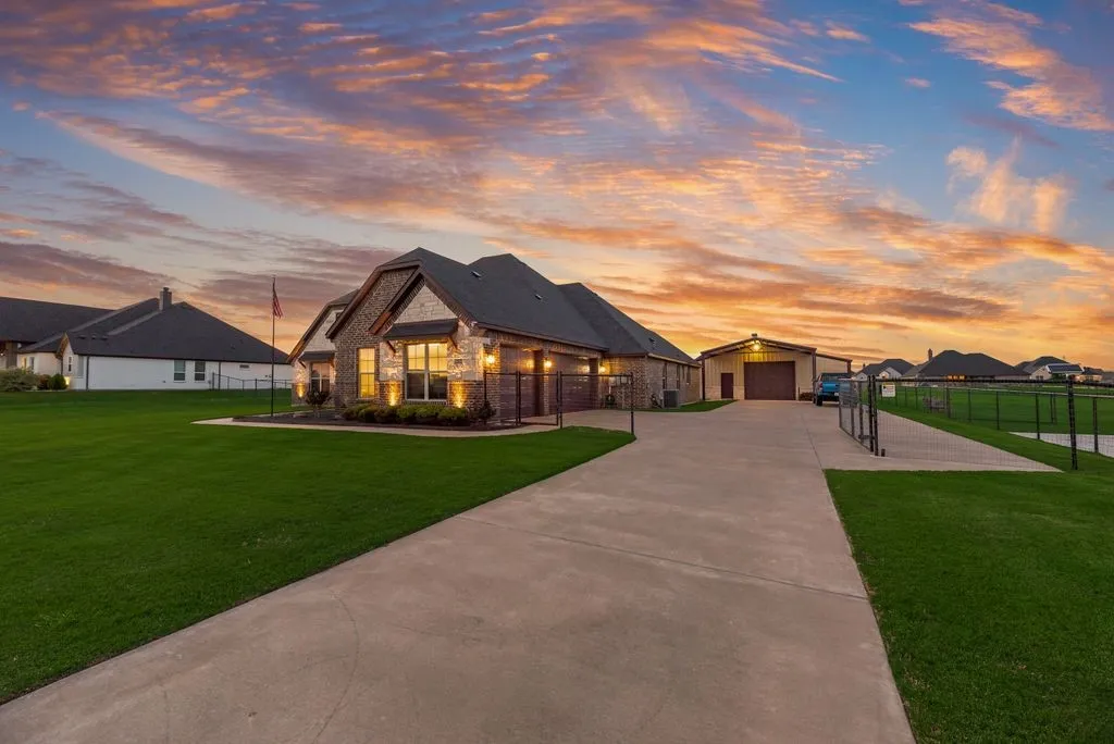 Stone and brick exterior featuring a multi-gable roof, expansive concrete driveway, detached garage with roll-up door, and extensive fenced yard space