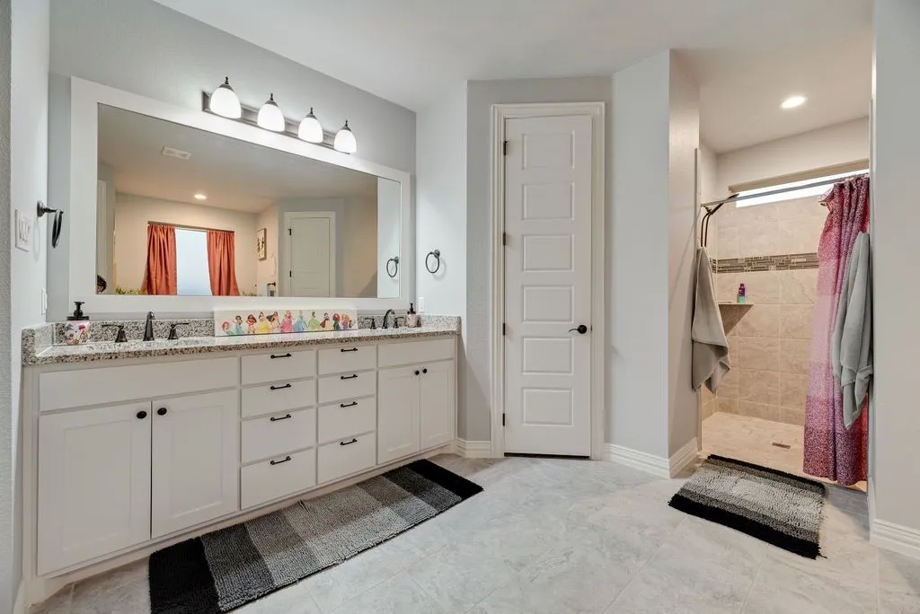 Bathroom featuring a double vanity with stone countertops, a large framed mirror, and white cabinetry