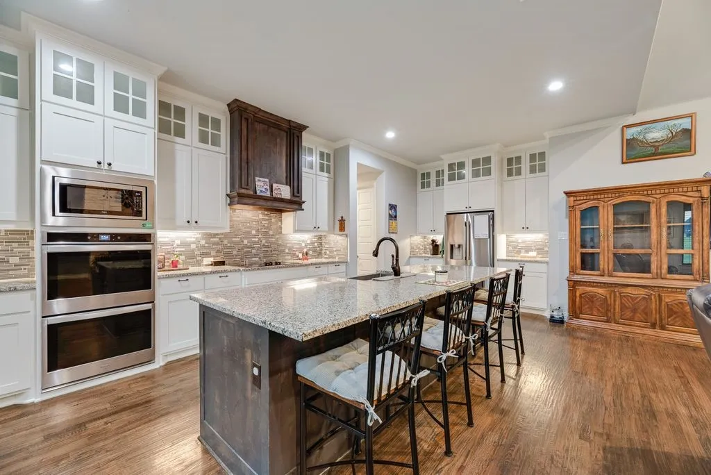 Kitchen featuring a large central island with seating, white cabinetry, dark wood-finish flooring, stainless steel appliances, and a tiled backsplash