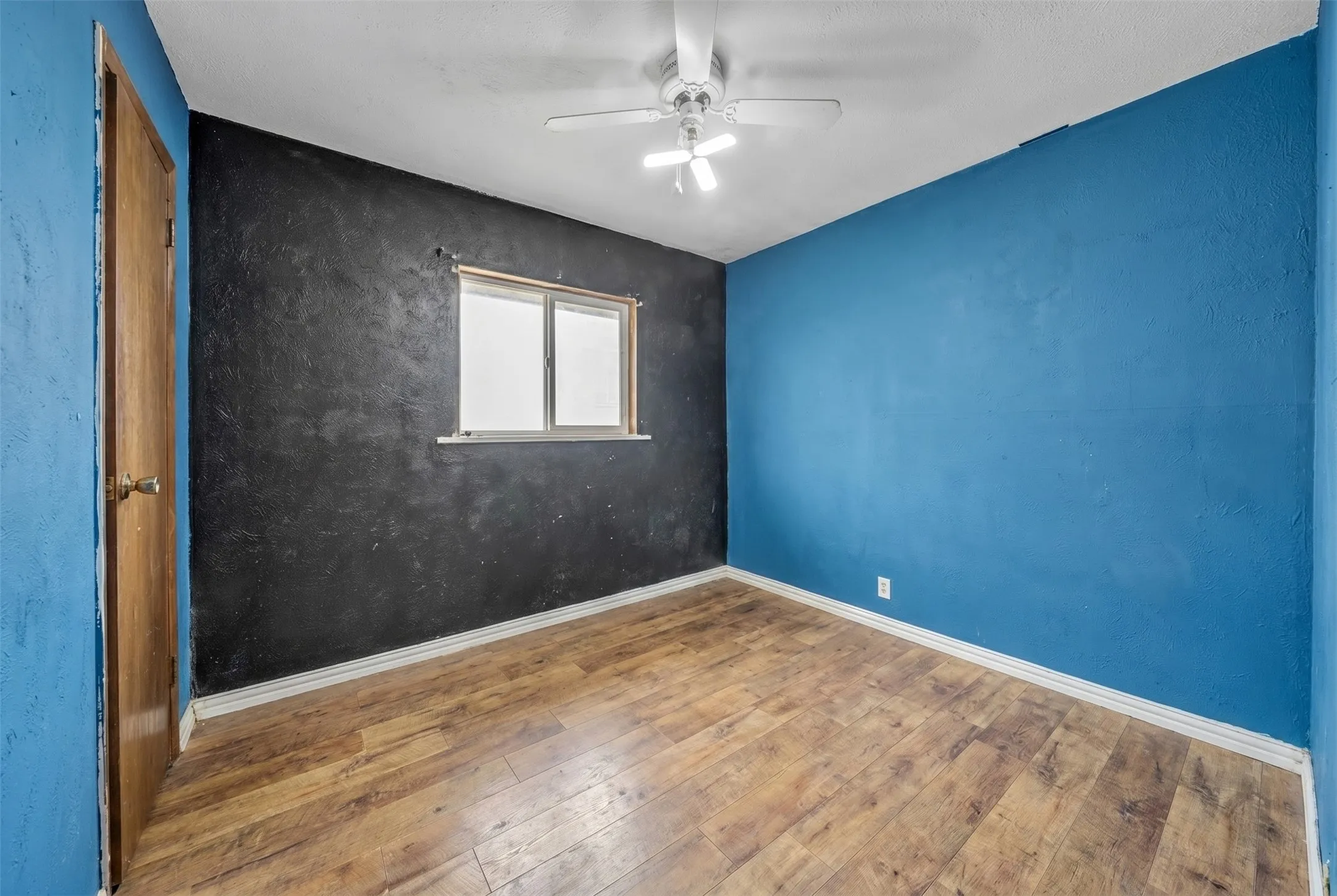 Room featuring wood-finish flooring, a ceiling fan with integrated lighting, and a double-pane window
