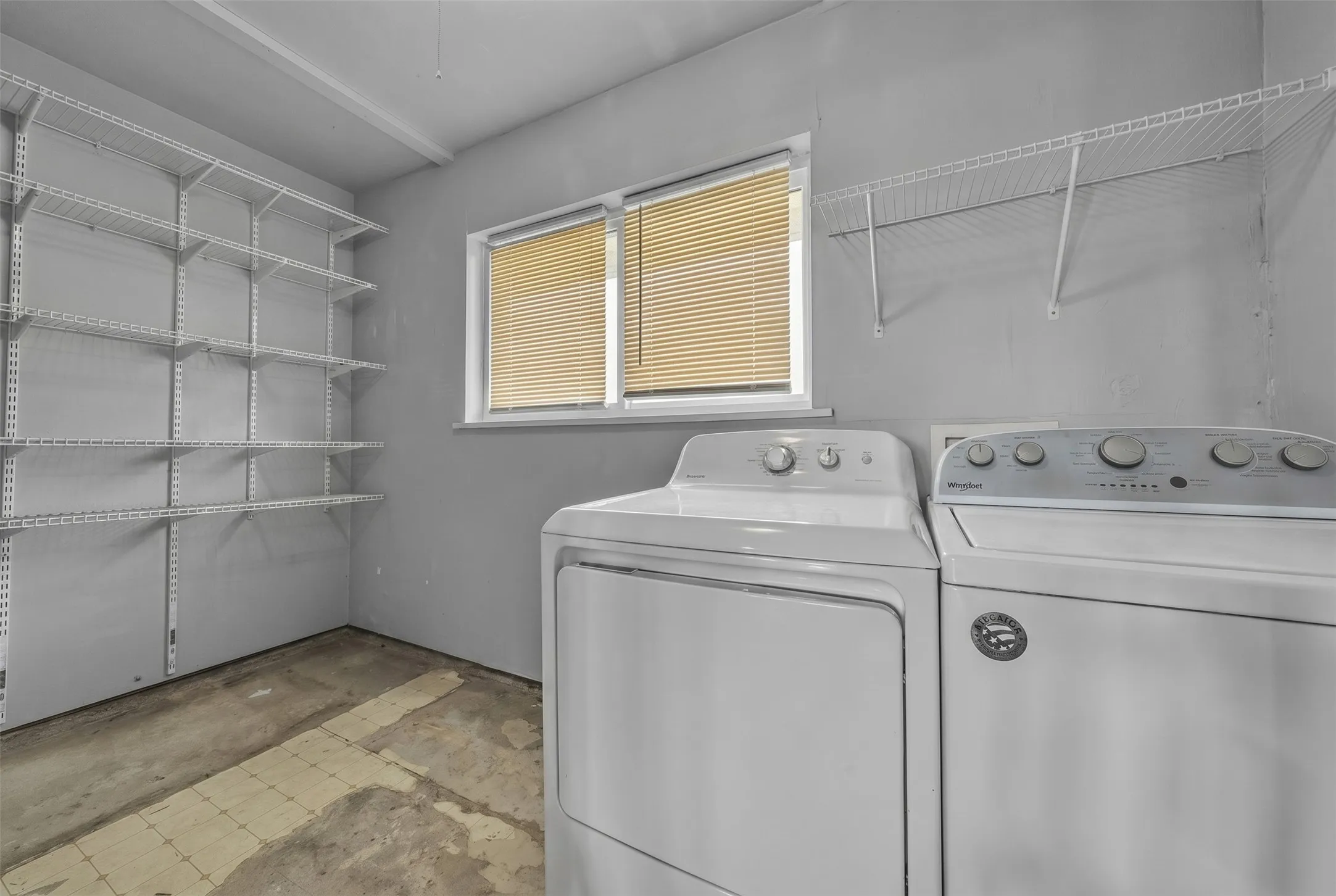 Utility space featuring extensive wire shelving, a window with horizontal blinds, and concrete flooring