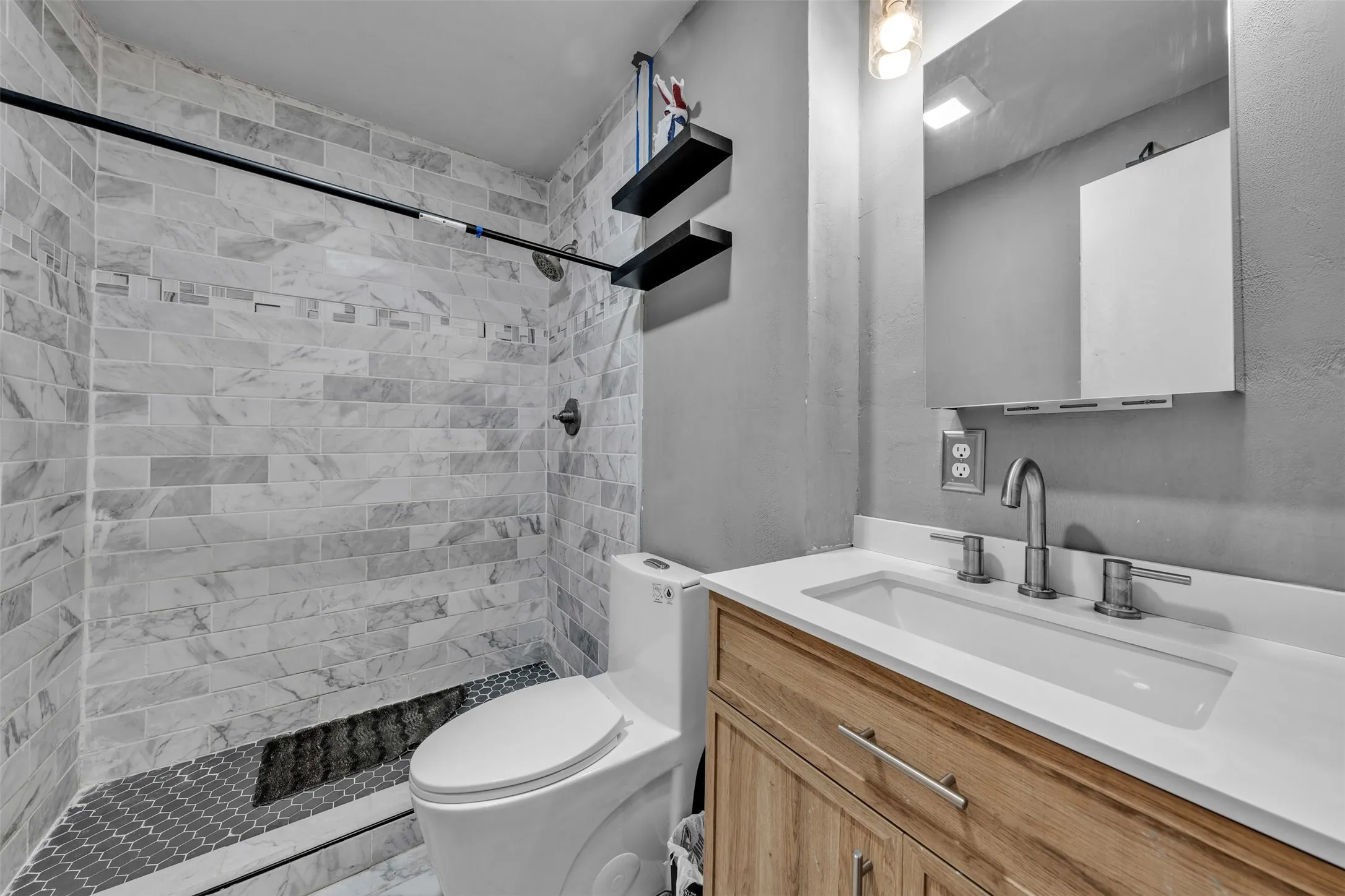 Bathroom featuring a walk-in shower with light-toned rectangular tile, a dark hexagon tile shower pan, a wall-mounted shower head, and a black shower rod