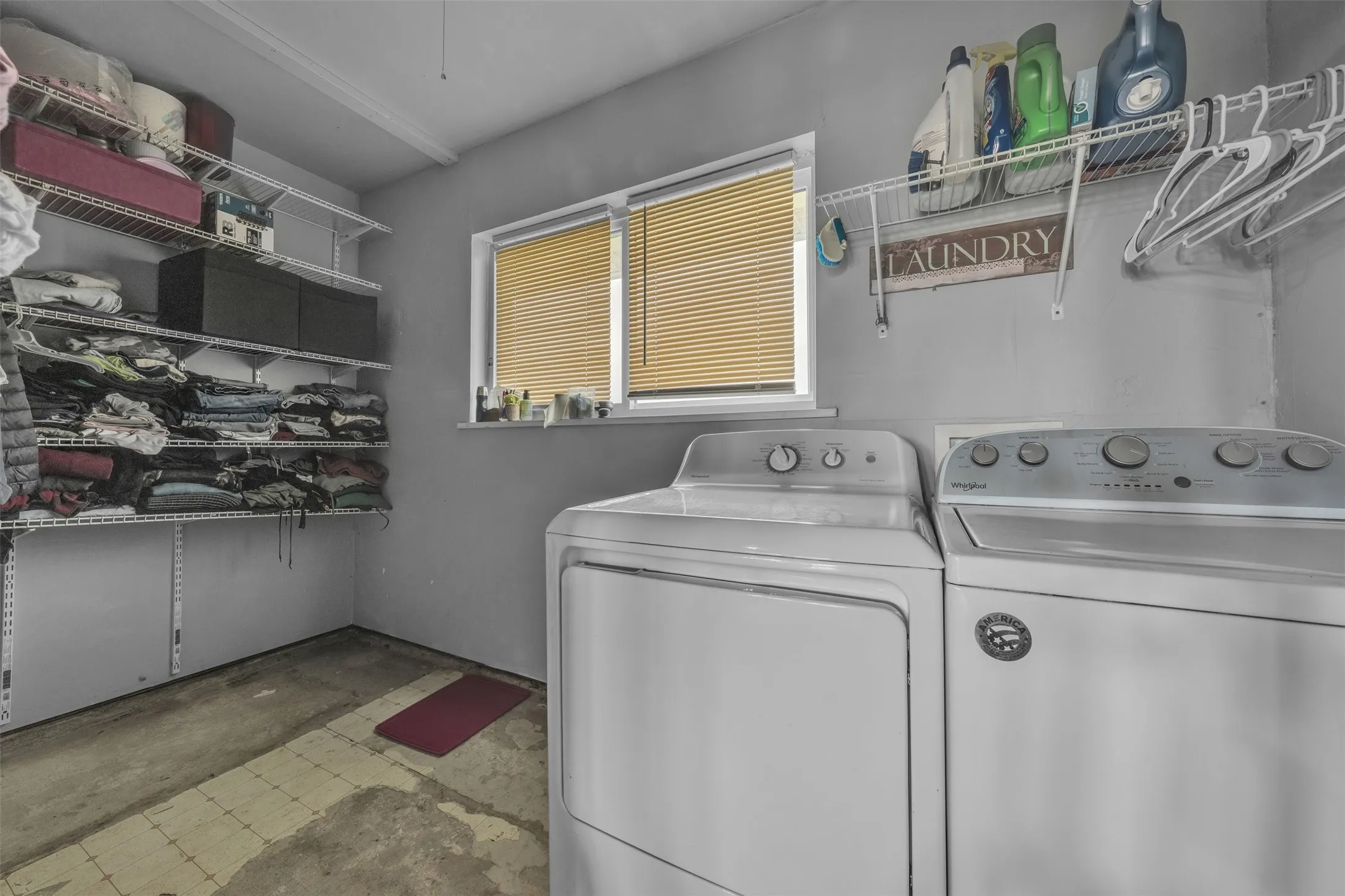 Utility room featuring a window with blinds, wall-mounted open shelving, and a washer and dryer