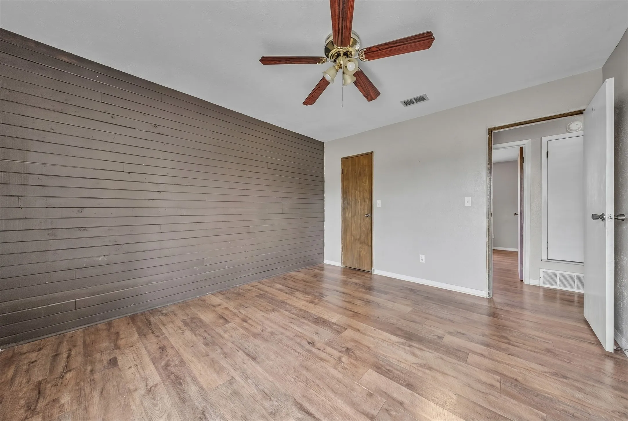 Interior space featuring wood-finish flooring, a plank accent wall, and a ceiling fan with wooden blades