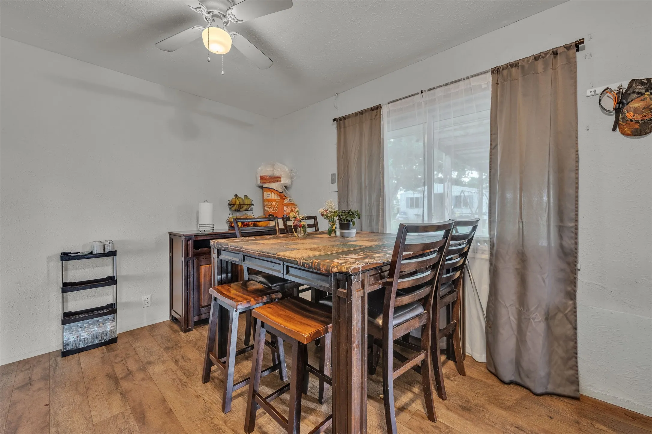 Dining area featuring wood-finish flooring, a ceiling fan with integrated lighting, and a large window with sheers
