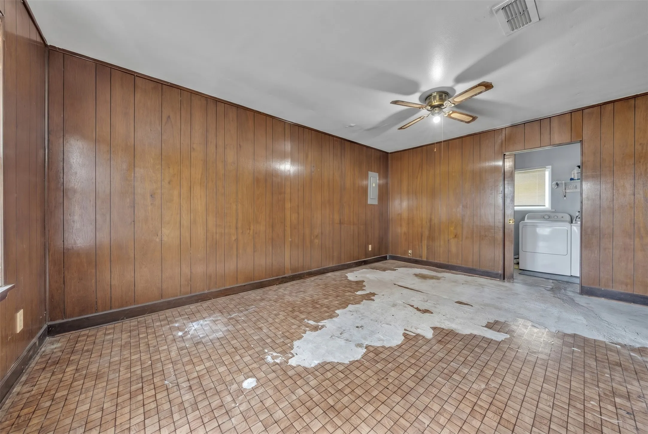 Room featuring wood-paneled walls, a ceiling fan with integrated lighting, and a patterned tile floor