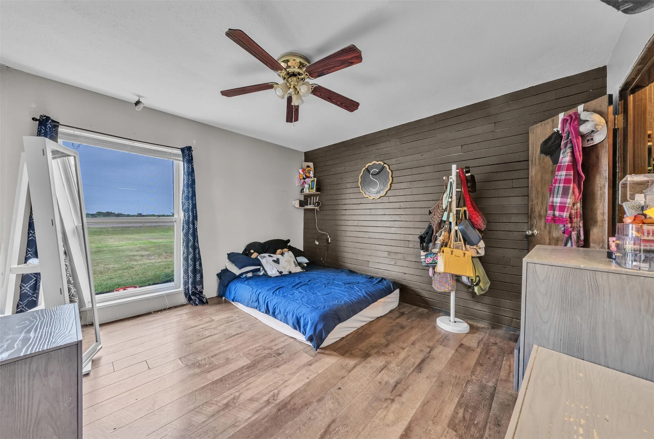 Bedroom featuring wood-finish flooring, a contemporary ceiling fan, and a prominent window with rural scenery
