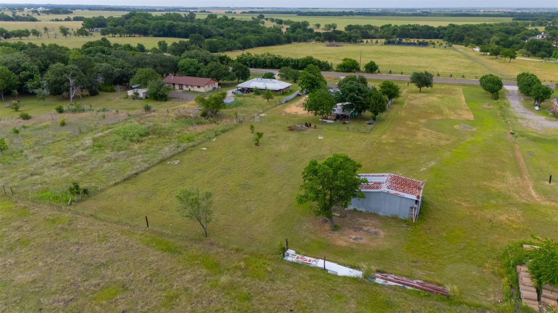 Expansive land parcel featuring multiple structures, open fields, mature trees, and a distant treeline