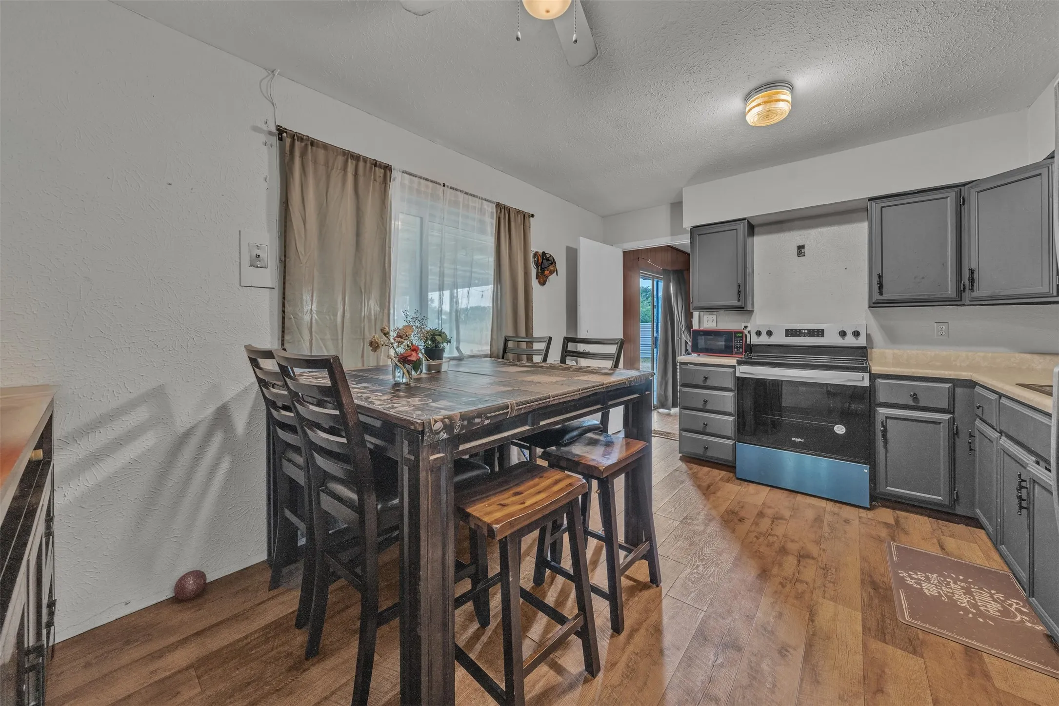 Kitchen featuring wood-finish flooring, dark cabinetry, light countertops, and a full suite of appliances including a range and microwave