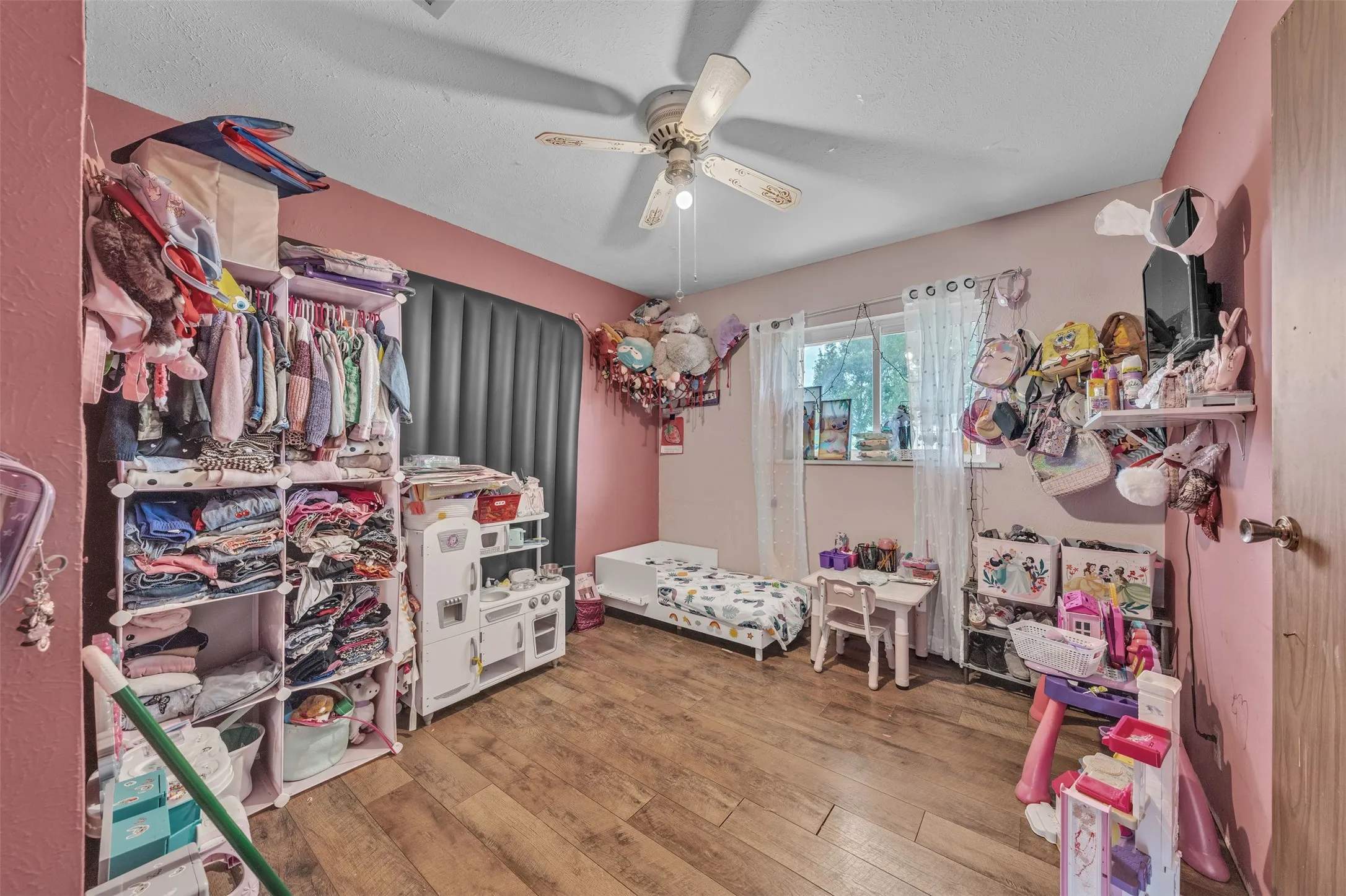 Room featuring wood-finish flooring, a ceiling fan with light fixture, and a window with sheer curtains