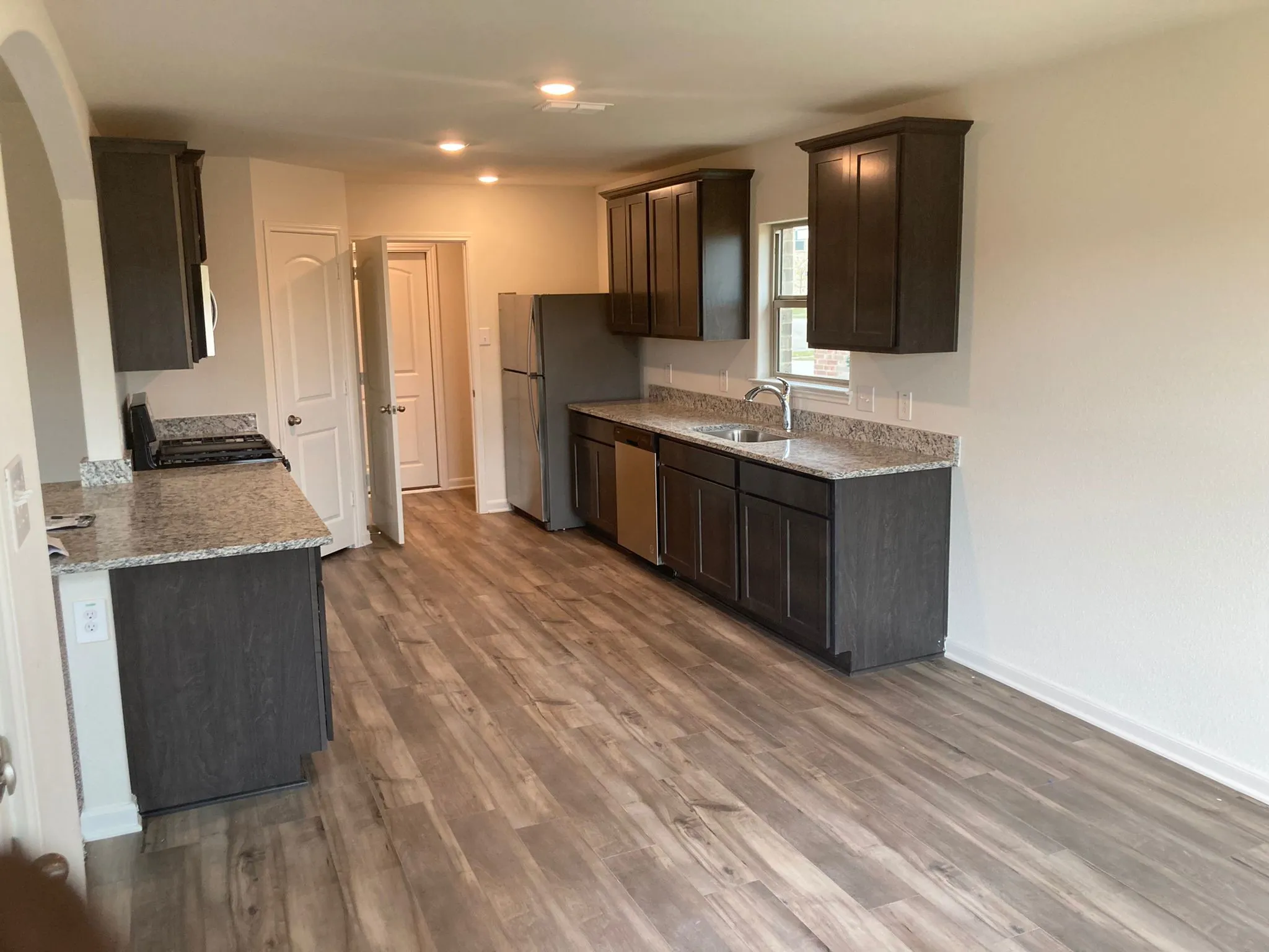 Kitchen featuring wood-finish flooring, dark wood-finish cabinetry, light stone-finish countertops, stainless steel appliances, and recessed lighting