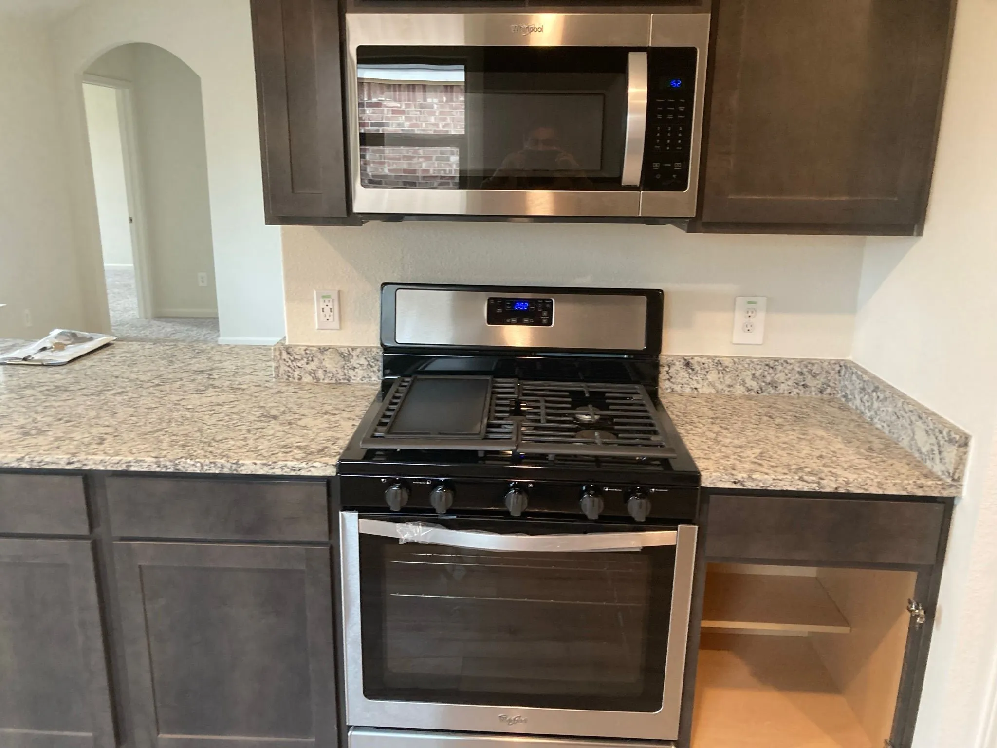 Kitchen featuring a stainless steel range with gas cooktop, built-in microwave, dark wood-finish cabinetry, and light-toned countertop with speckled pattern