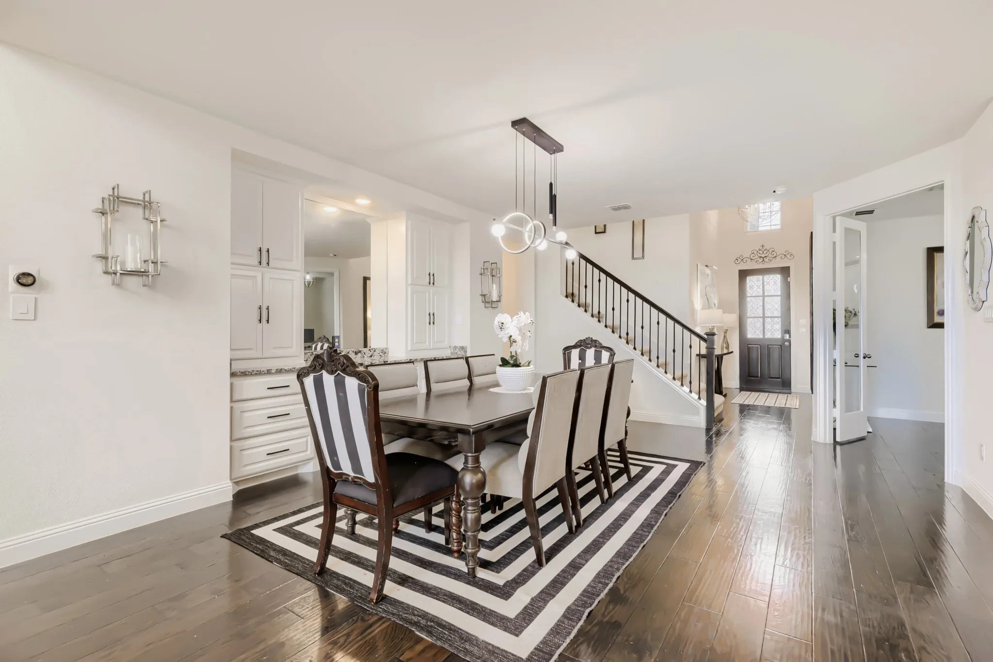 Open-concept dining area featuring dark wood-finish flooring, a modern linear pendant light fixture, and a built-in buffet with upper cabinetry and a stone countertop