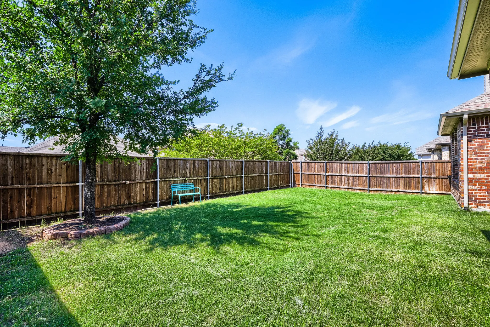 Expansive backyard featuring a lush green lawn, mature shade tree with a brick-lined bed, and a full privacy fence