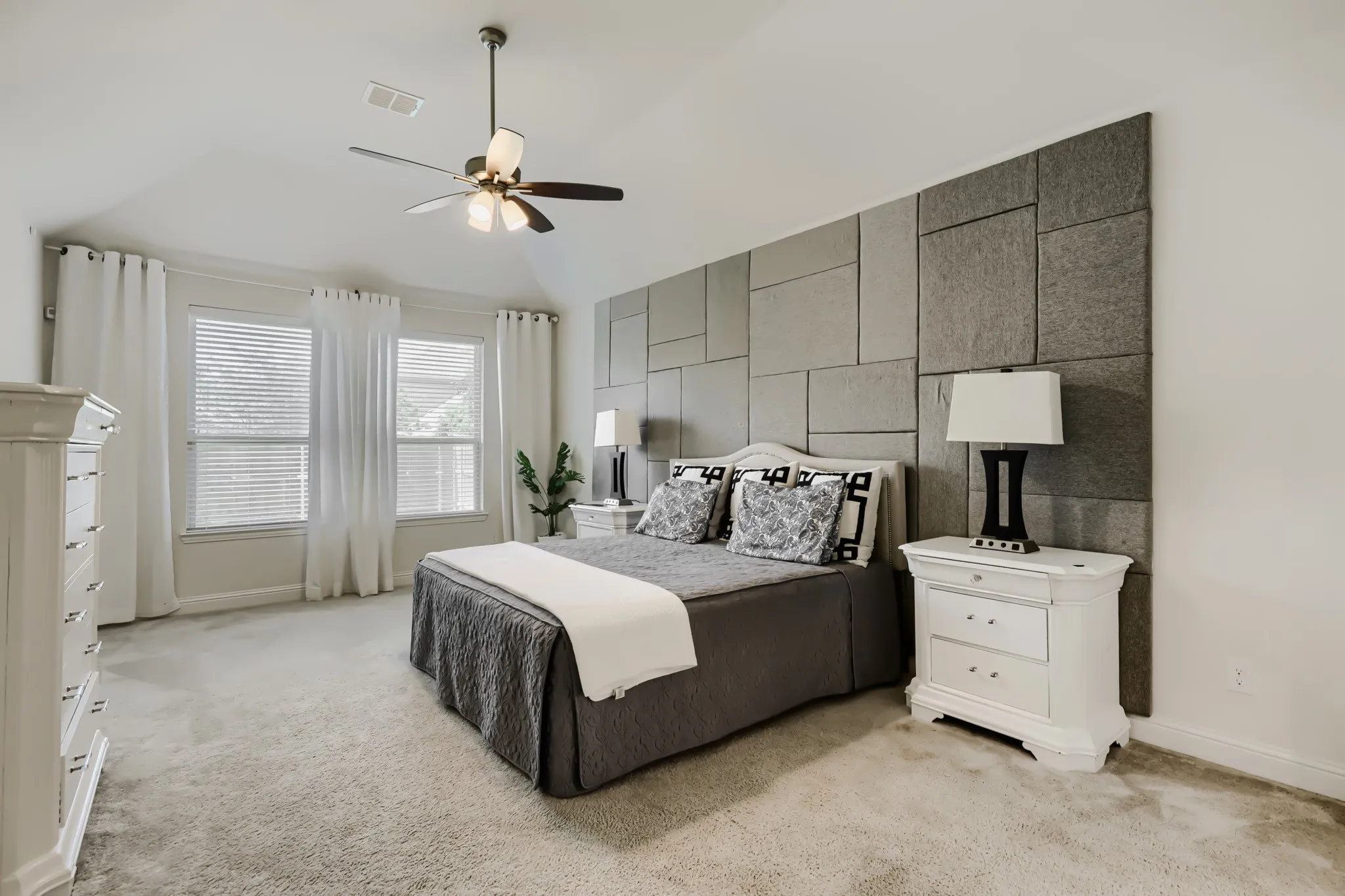 Carpeted room featuring a ceiling fan with integrated lighting, a paneled accent wall, and two large windows