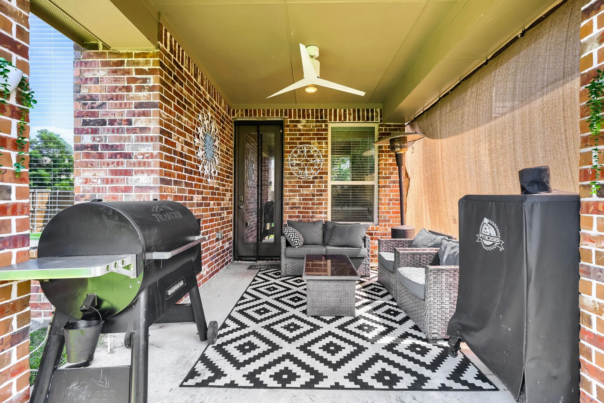 Covered patio featuring brick exterior walls, a ceiling fan, concrete flooring, and a privacy screen