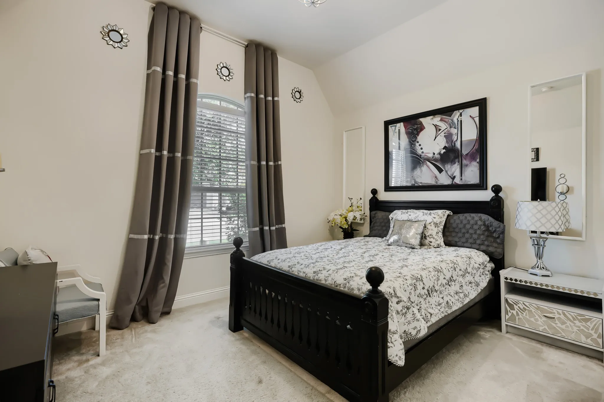 Bedroom featuring a large arched window with blinds, light-toned carpeting, and light-colored walls