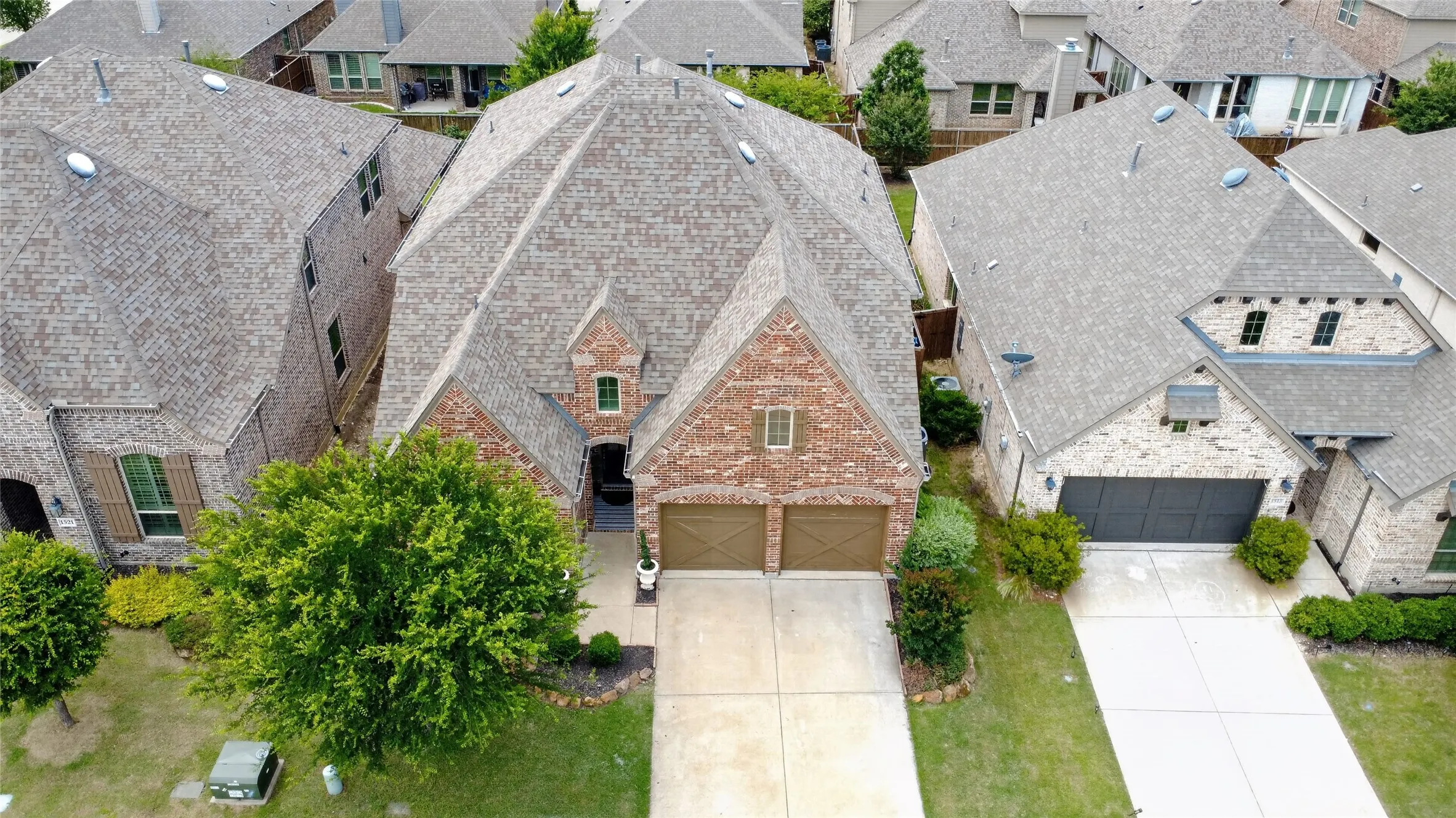 Brick facade residence featuring a multi-gabled roofline, an attached two-car garage with wood-finish doors, a concrete driveway, and mature landscaping