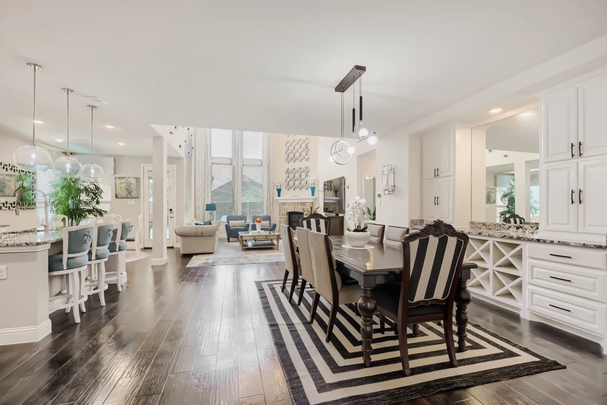 Open-concept living space featuring wood-finish flooring, a built-in wet bar with granite countertops and integrated wine storage, and a dining area with contemporary lighting