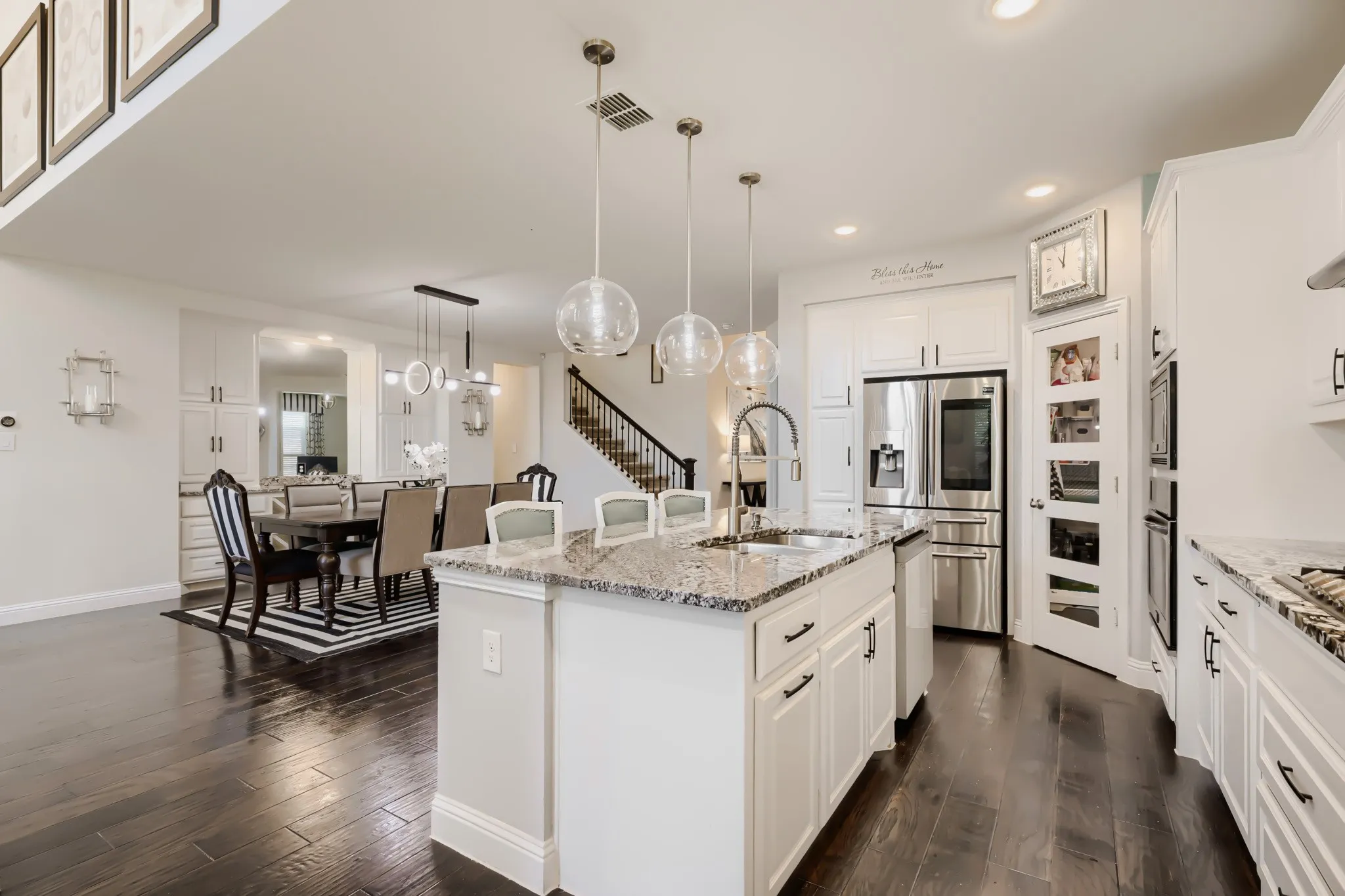 Gourmet kitchen featuring a central island with granite countertops, stainless steel appliances, white cabinetry with dark hardware, and dark wood-finish flooring