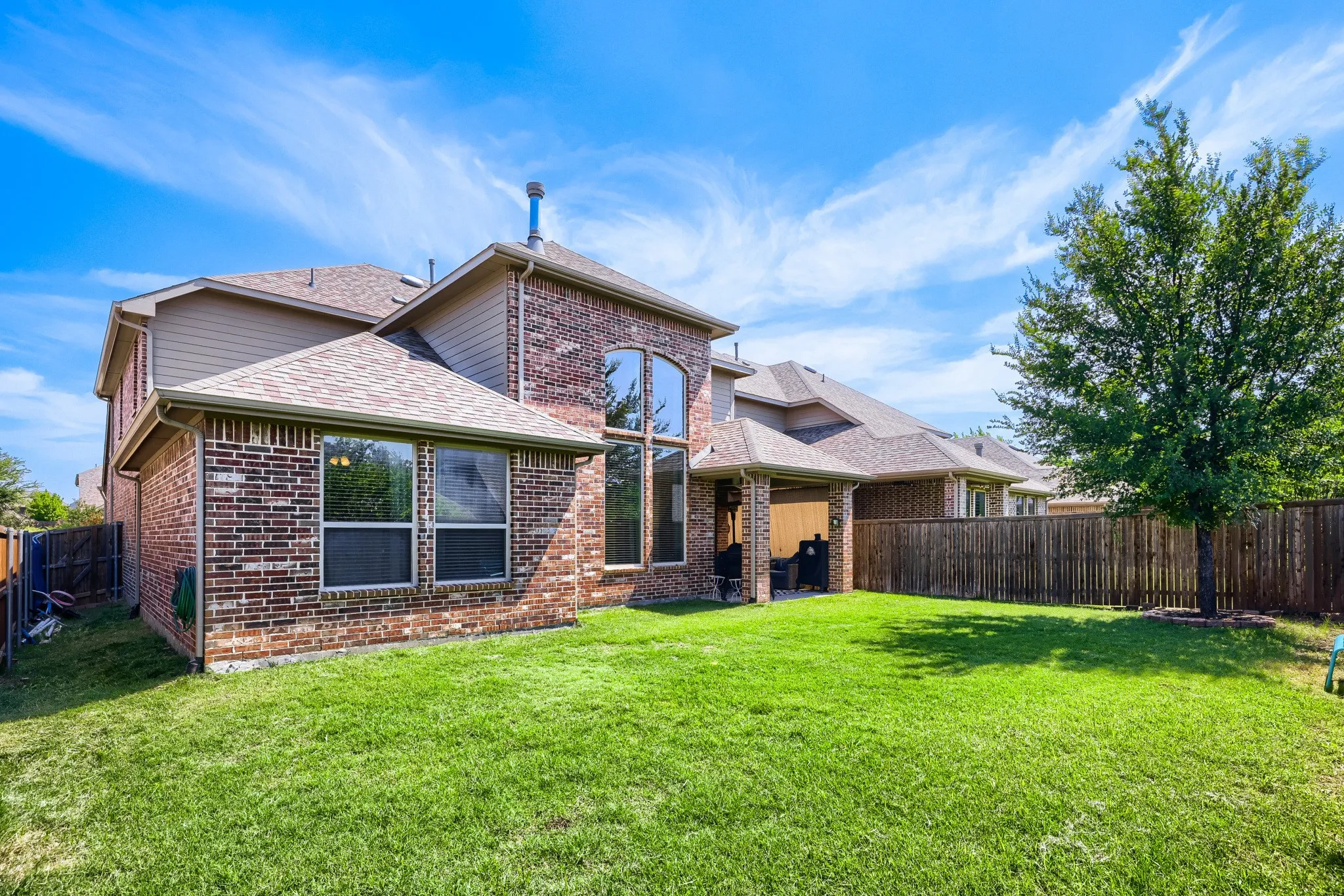 Spacious backyard with a vibrant green lawn, featuring a covered patio, privacy fencing, and a mature tree