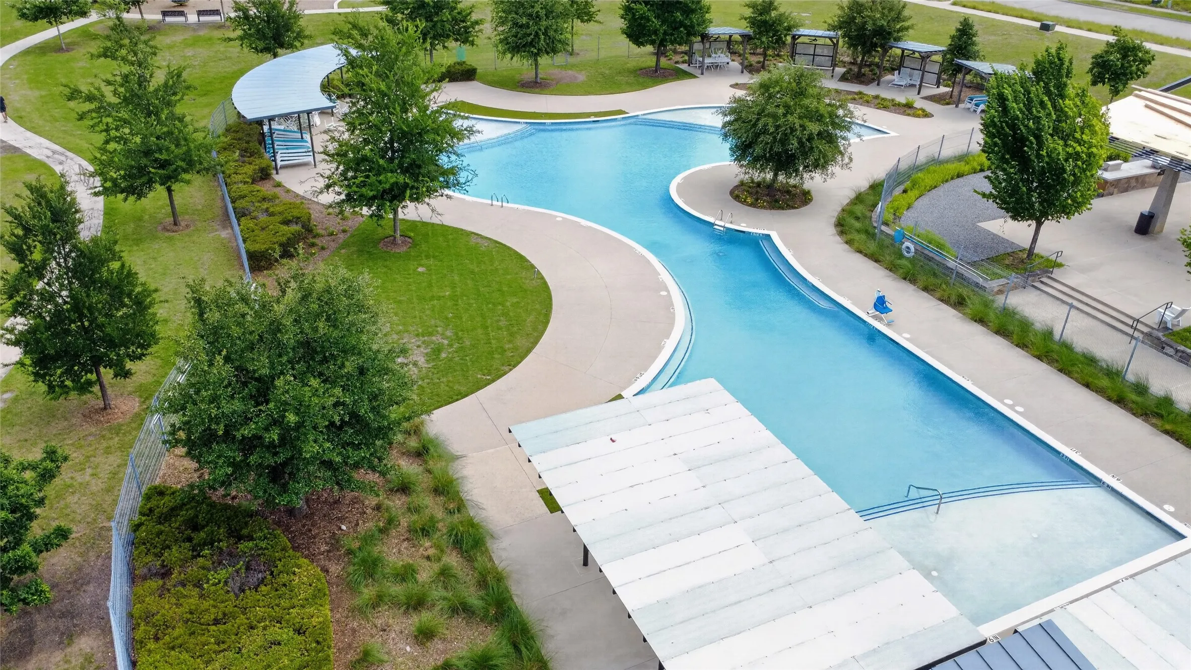 Expansive resort-style pool featuring multiple swimming areas, integrated lounge spaces, a winding design, and surrounding concrete decking