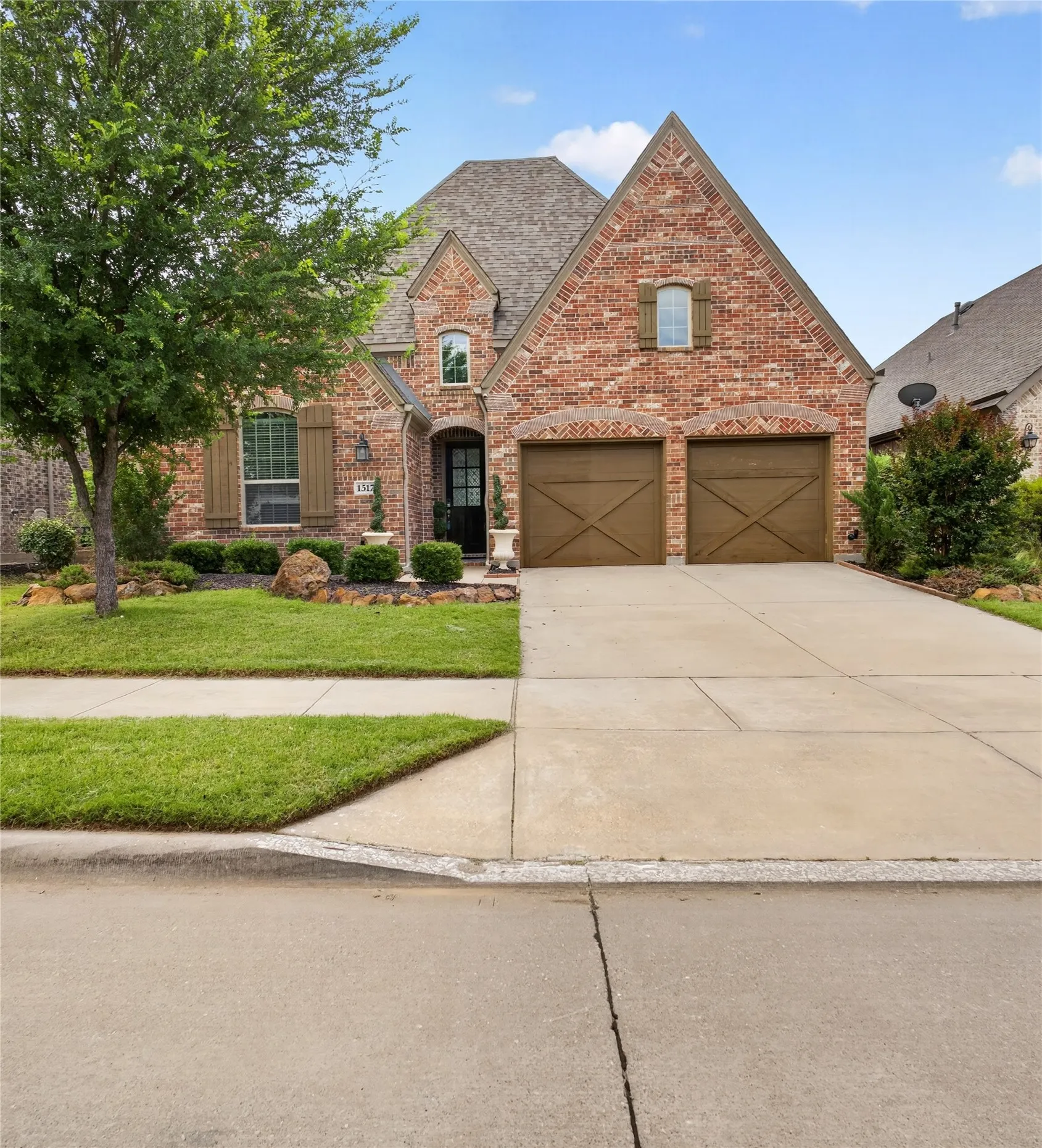 Brick facade residence featuring a front-facing attached two-car garage with wood-finish doors