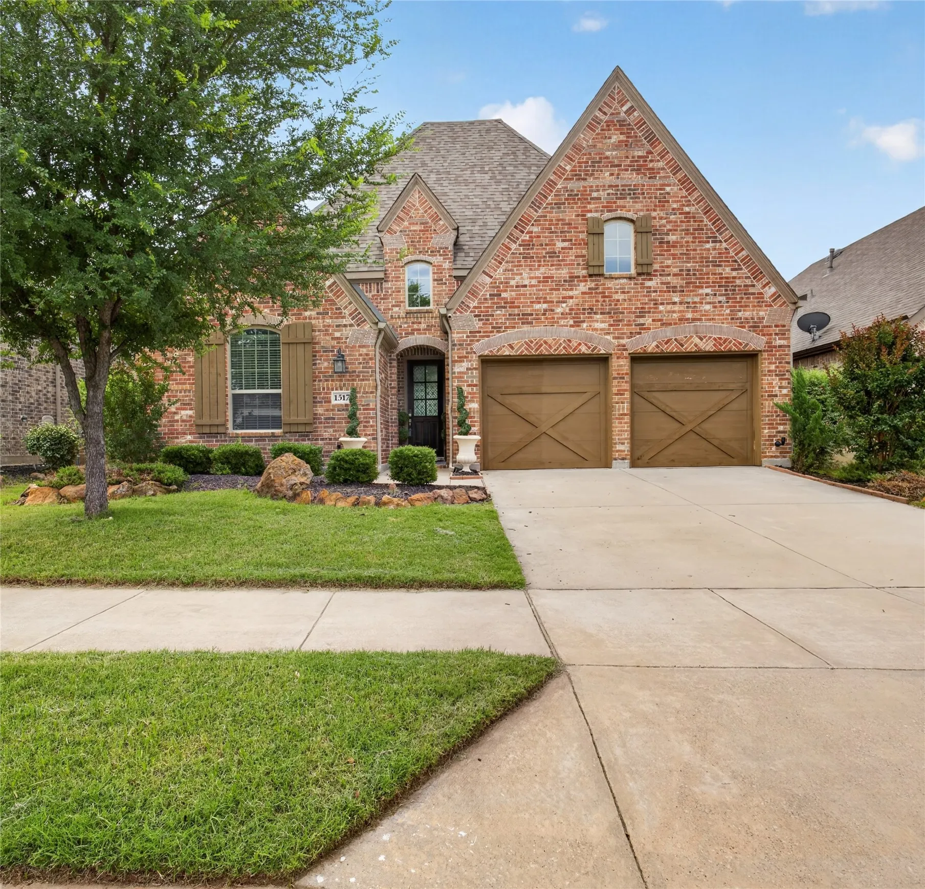Brick facade residence featuring a covered entry, decorative wood shutters, and an attached two-car garage with carriage-style doors