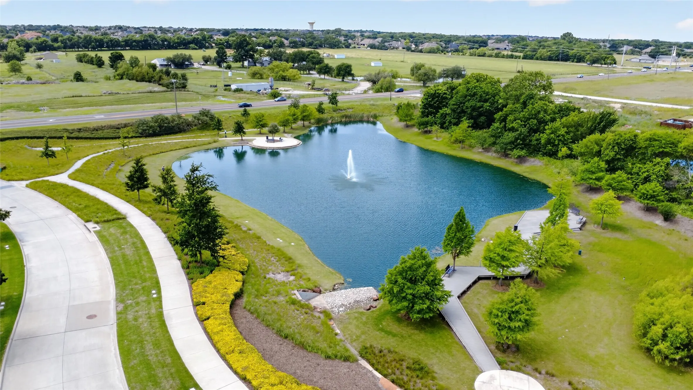 Community water feature with aeration fountain, surrounded by manicured grounds, paved walkways, and mature landscaping