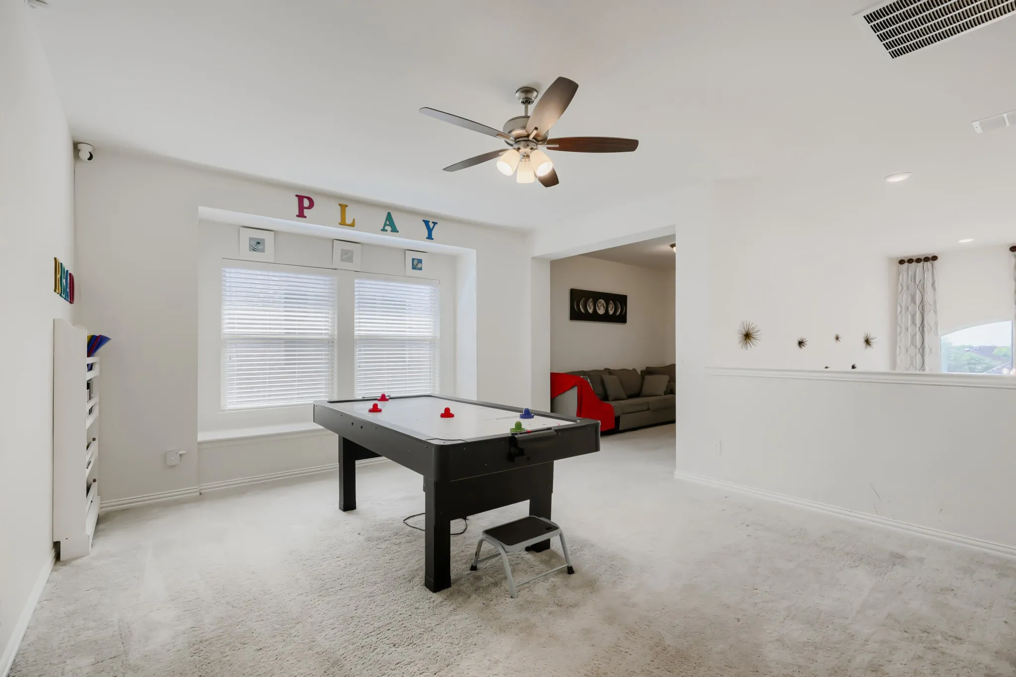 Carpeted room with a ceiling fan light fixture, white walls, and a large window featuring horizontal blinds and a window seat