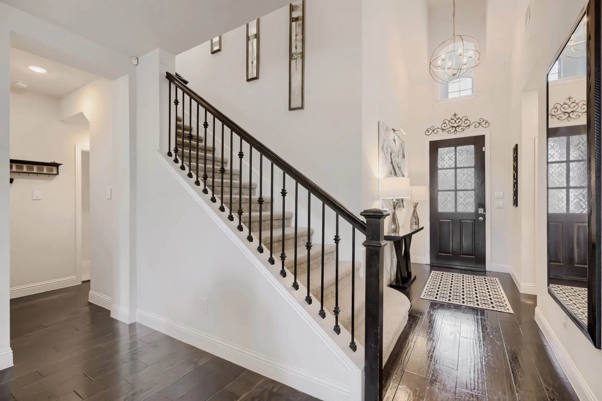 Foyer featuring a dark wood-finish front door with decorative glass panels, double-height ceiling, large spherical chandelier, dark wood-finish flooring, and a carpeted staircase with dark iron balusters